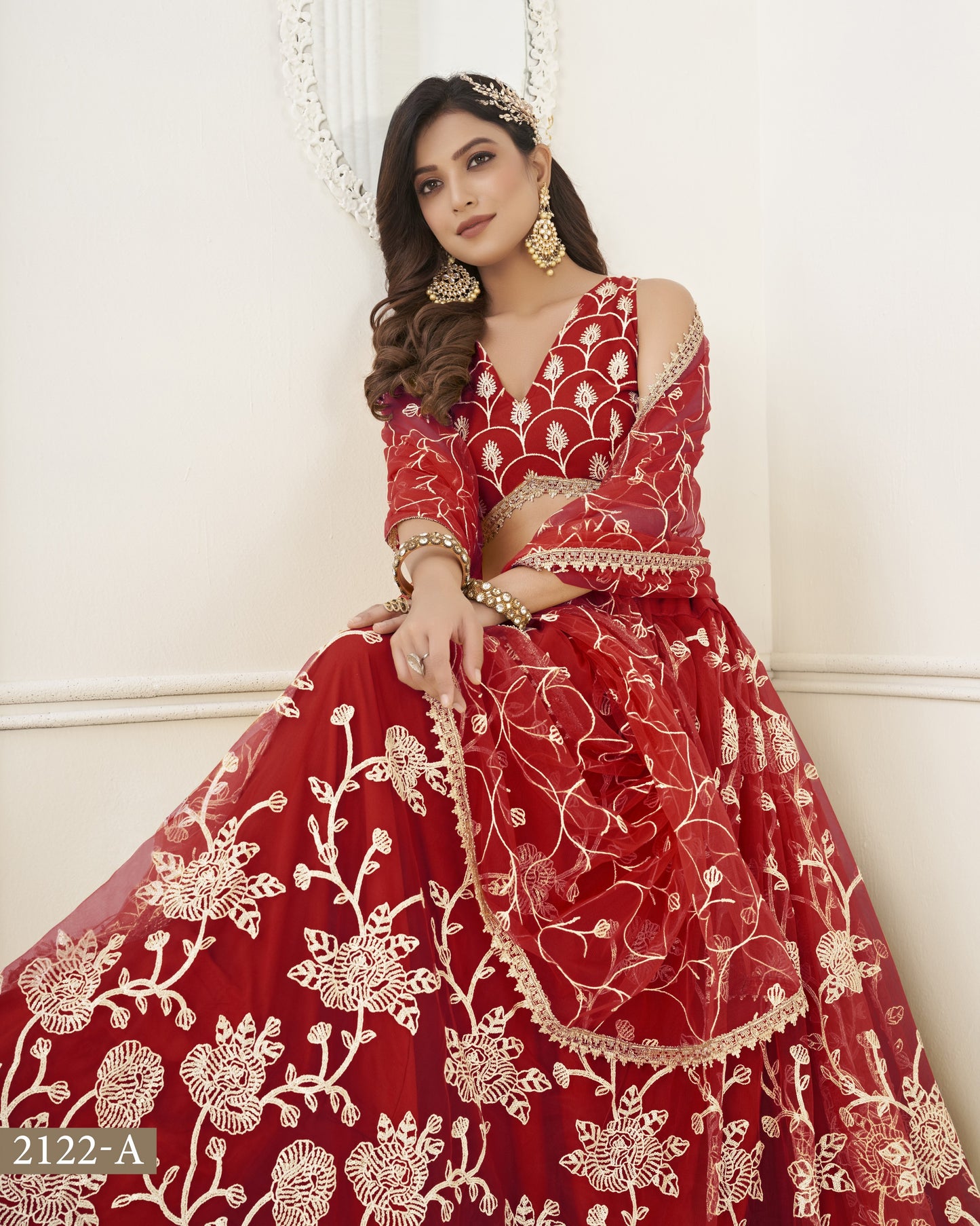 Woman wearing a red embroidered traditional outfit with gold jewelry against a white background