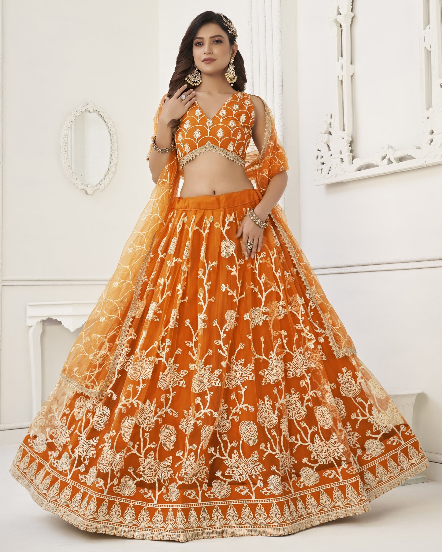 Woman wearing an orange embroidered traditional outfit in a white room.