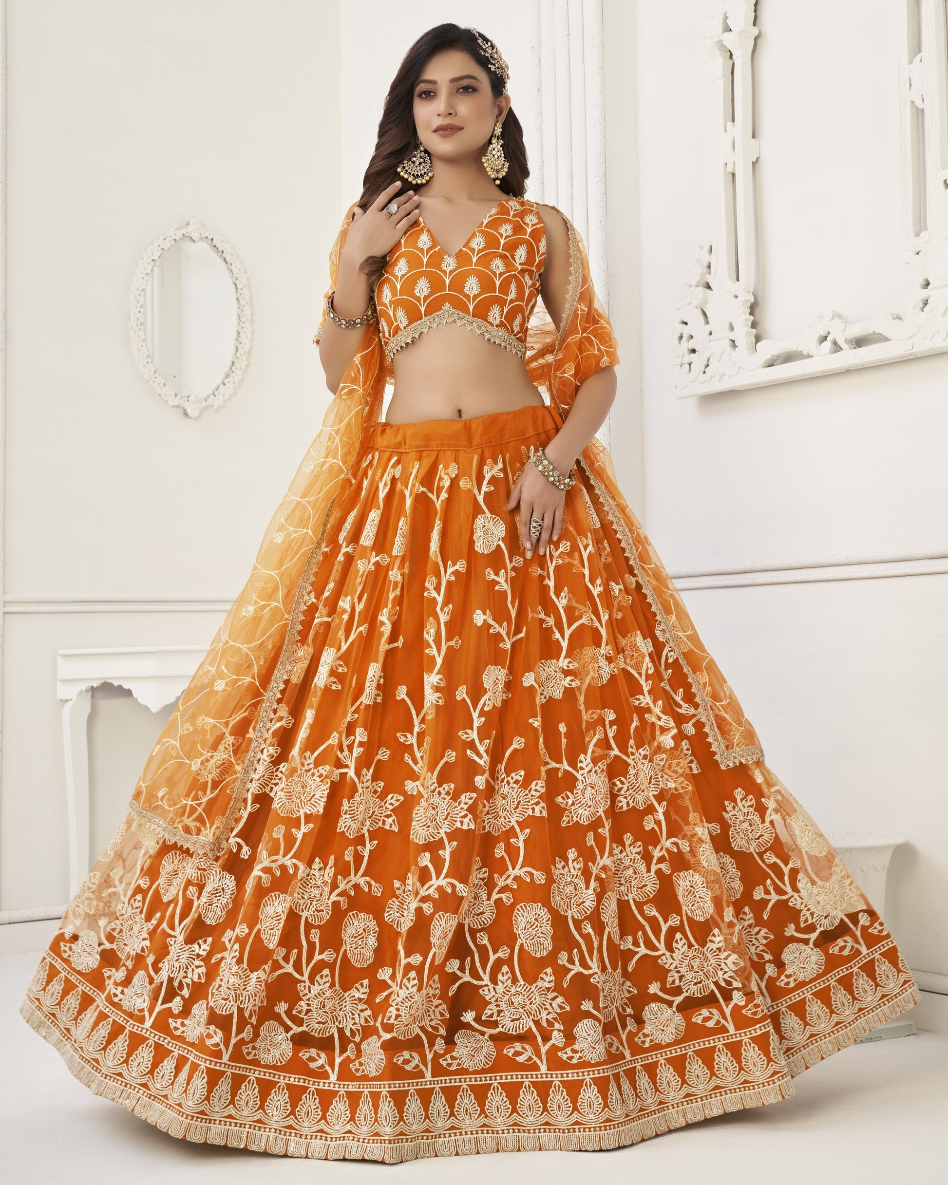 Woman wearing an orange embroidered traditional outfit in a white room.