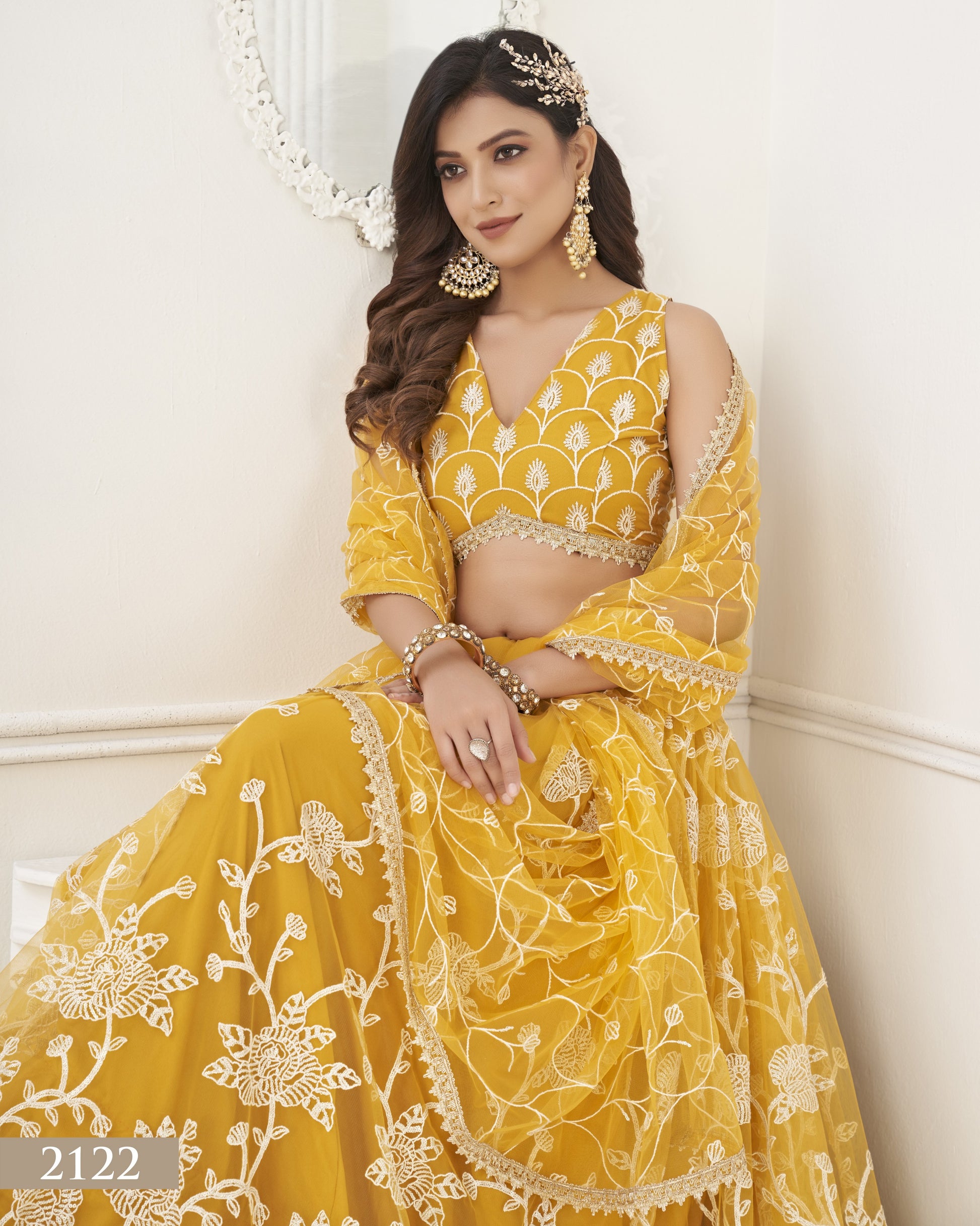 Woman wearing a yellow embroidered traditional outfit with gold jewelry against a white background