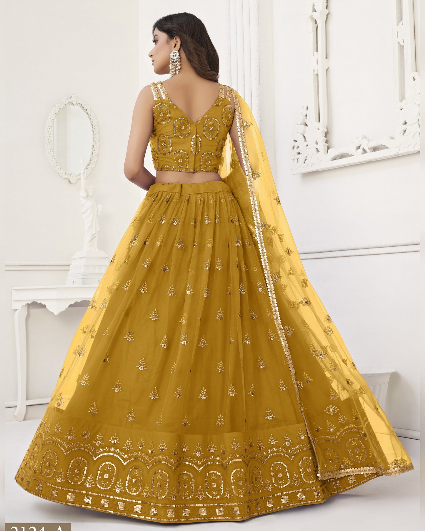 Woman wearing a yellow embroidered traditional outfit in a white room.