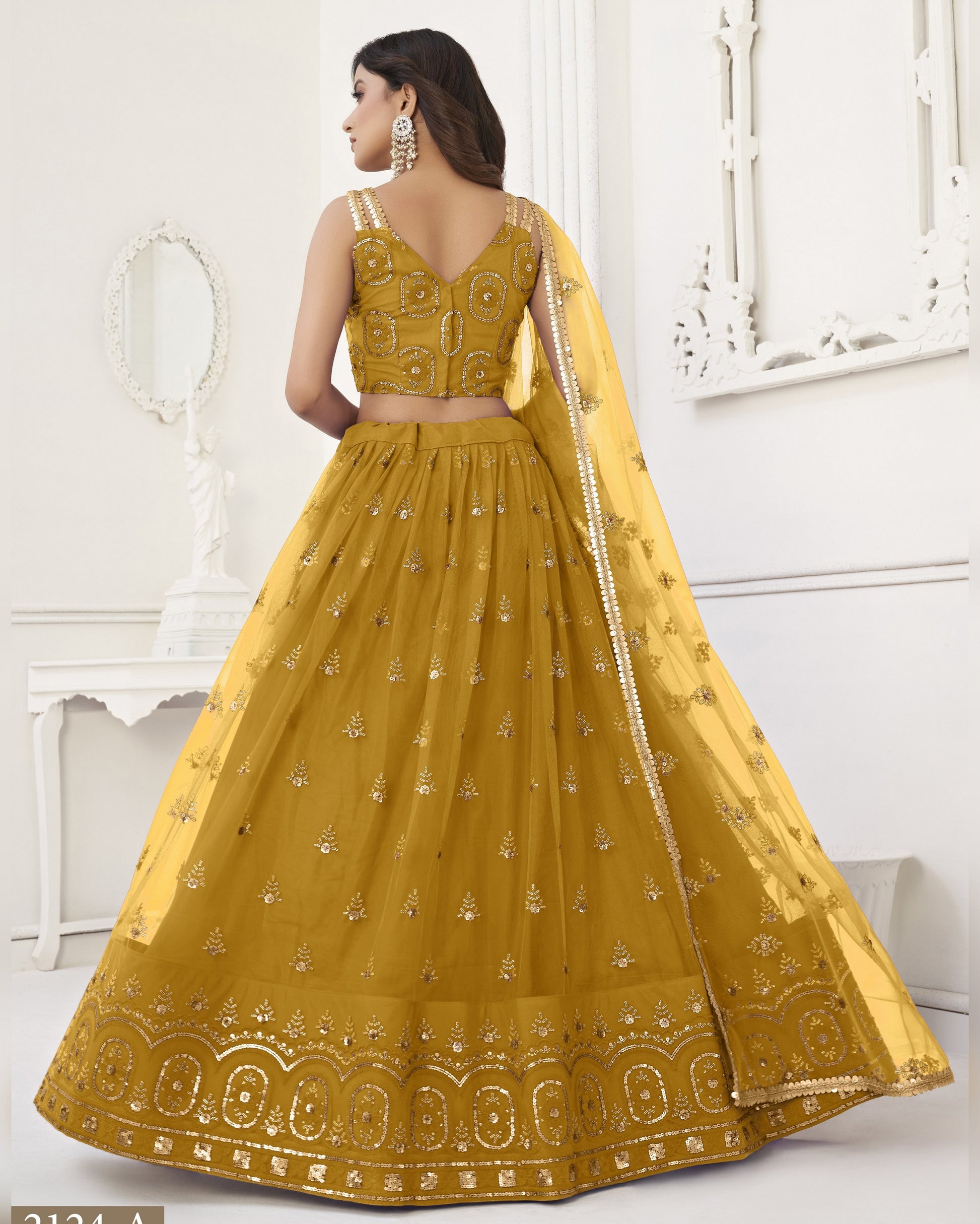 Woman wearing a yellow embroidered traditional outfit in a white room.