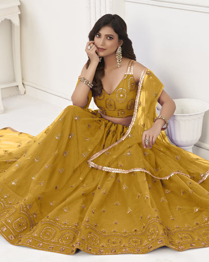 Woman in a yellow traditional outfit with intricate designs, sitting on a white surface.
