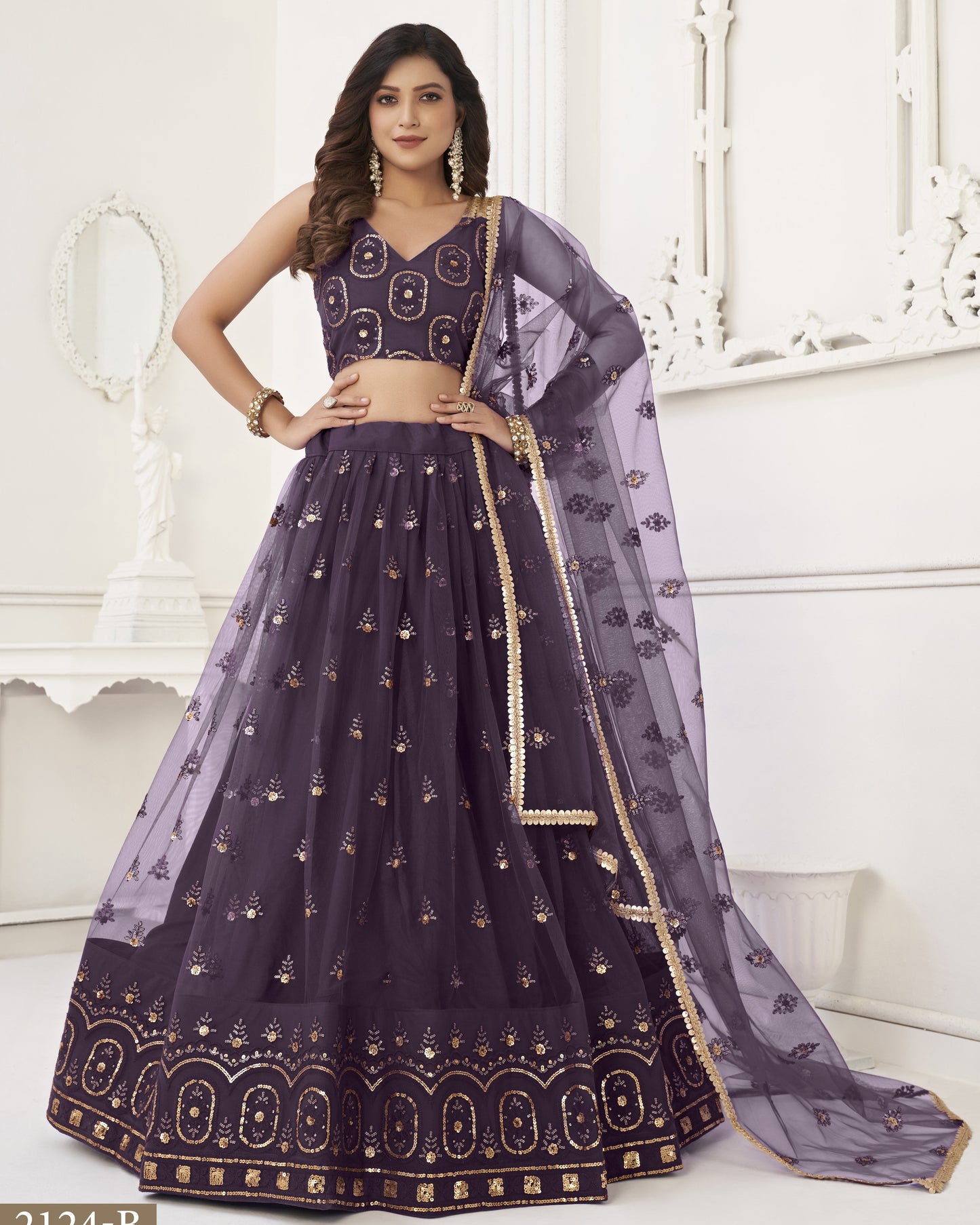 Woman wearing a dark purple embroidered lehenga with gold details in a white room.
