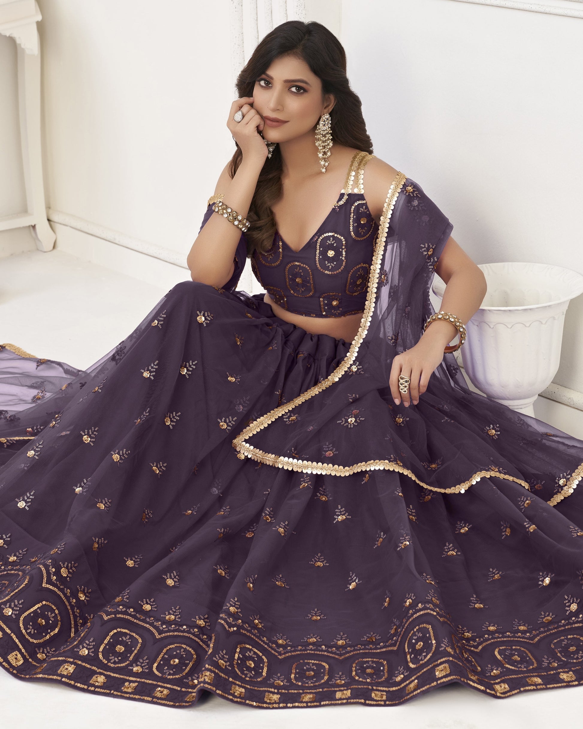 Woman in a purple embroidered traditional outfit sitting on a white surface.