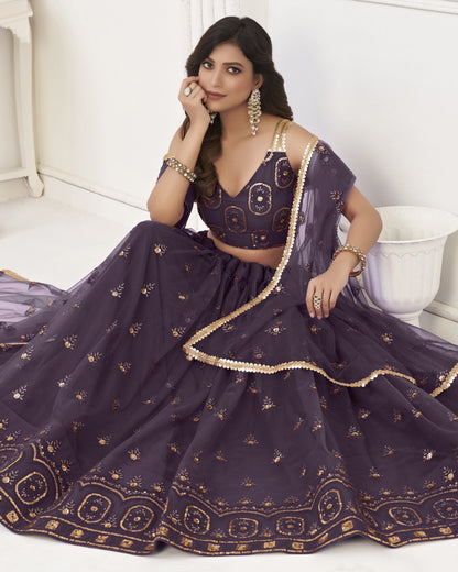 Woman in a purple embroidered traditional outfit sitting on a white surface.