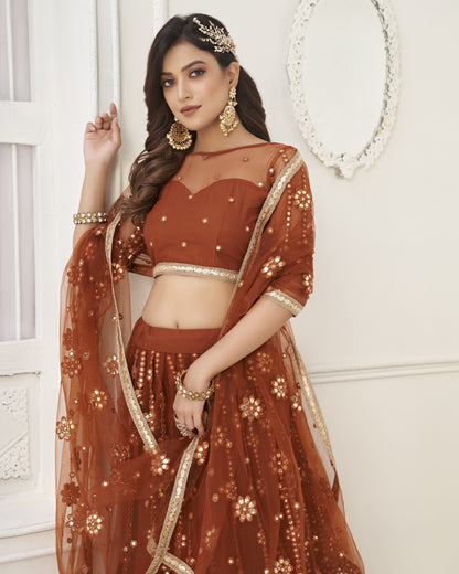 Woman in a traditional brown outfit with gold details against a white wall.