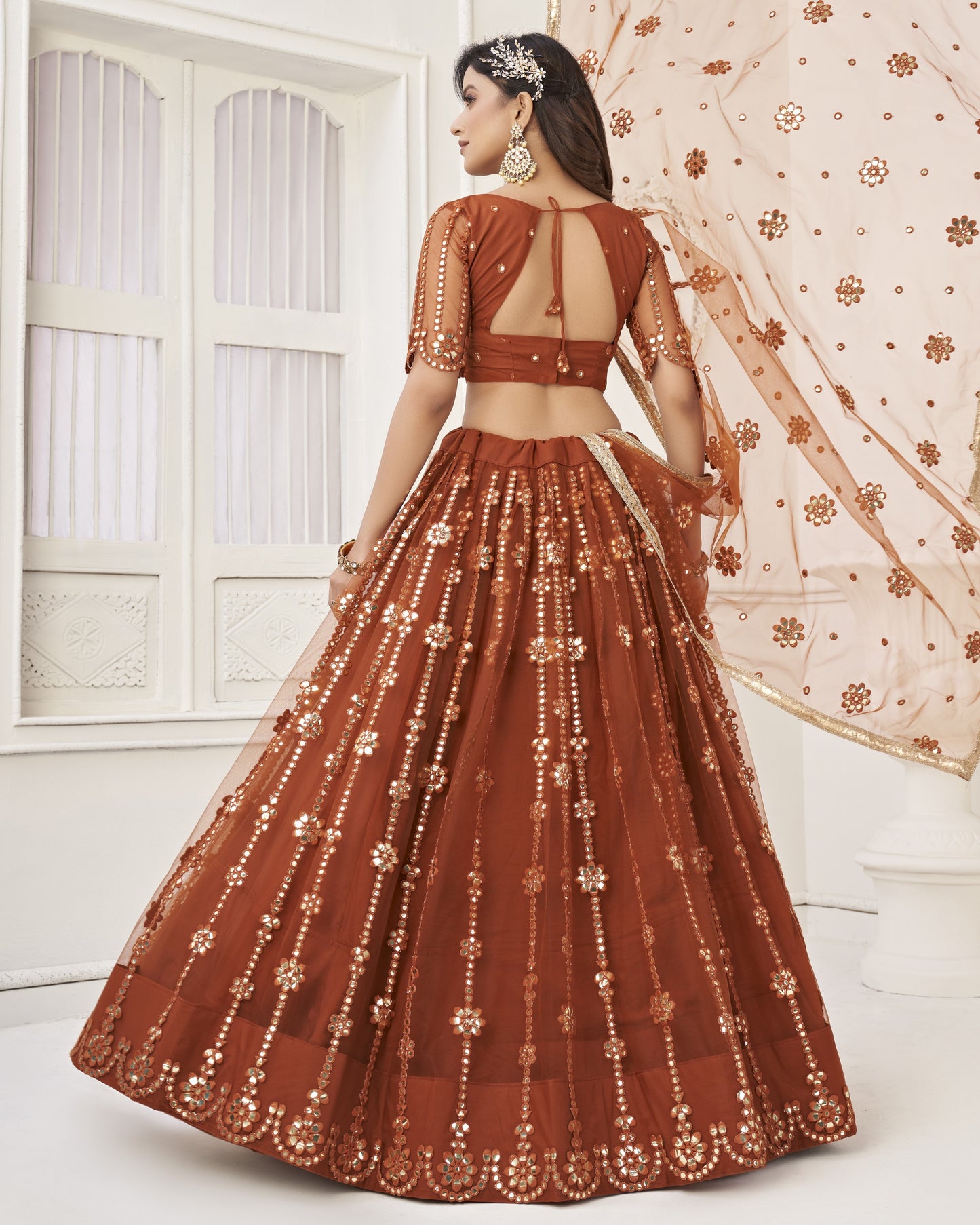 Woman wearing a brown embroidered traditional outfit with a sheer dupatta in a bright setting.
