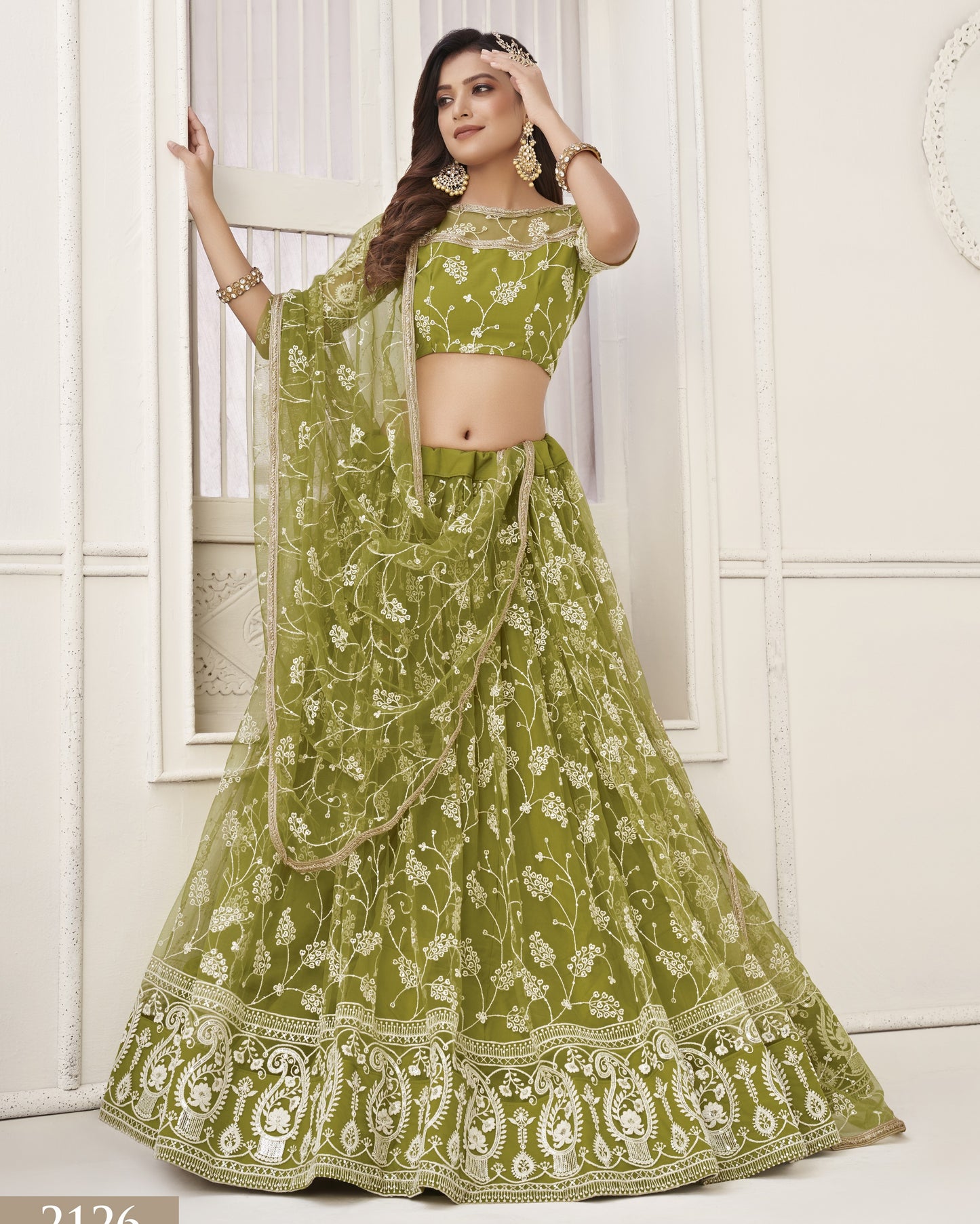 Woman wearing a green embroidered lehenga with a matching blouse in a white room.