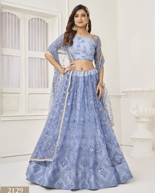 Woman wearing a blue embroidered lehenga with a matching blouse in a white room.
