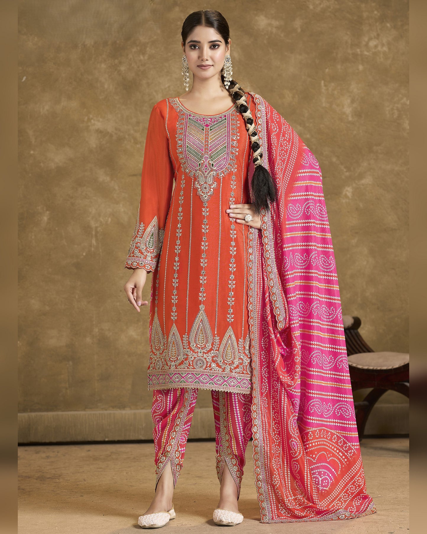 Woman wearing a traditional outfit with a red and pink dupatta against a brown background