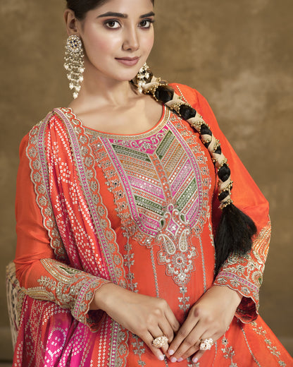 Woman wearing an orange and pink embroidered traditional outfit with jewelry against a brown background