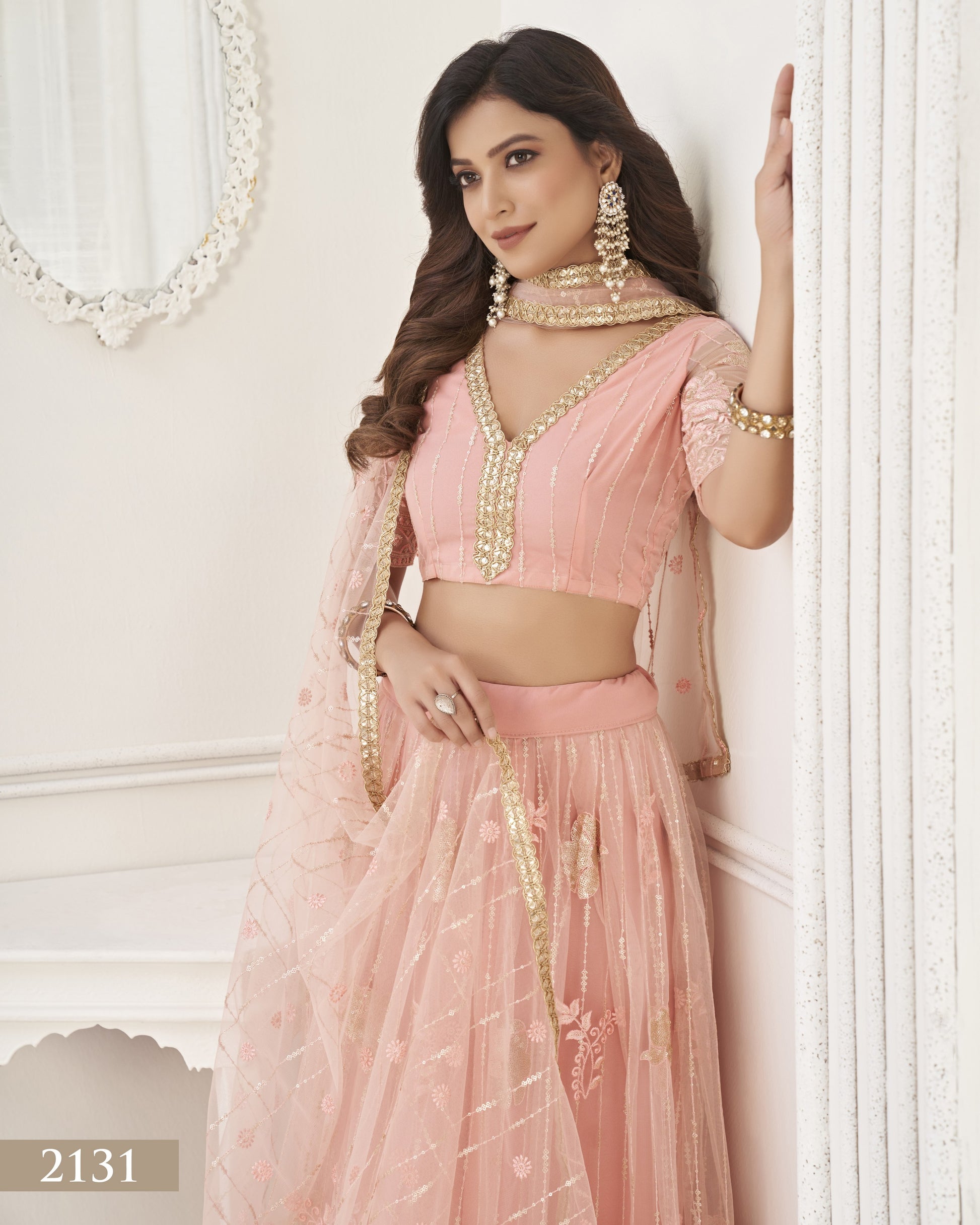 Woman in a pink traditional outfit with gold details against a white wall.