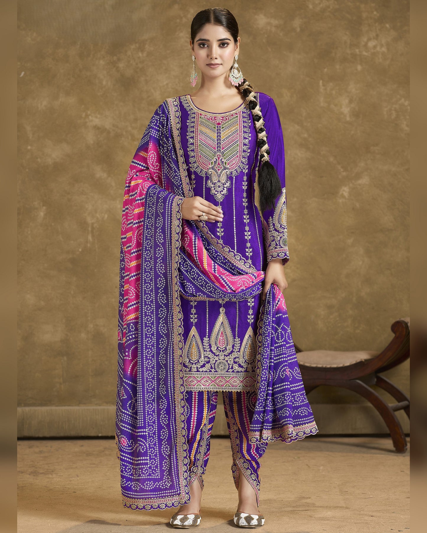 Woman wearing a traditional embroidered outfit with a purple and pink design against a beige background.