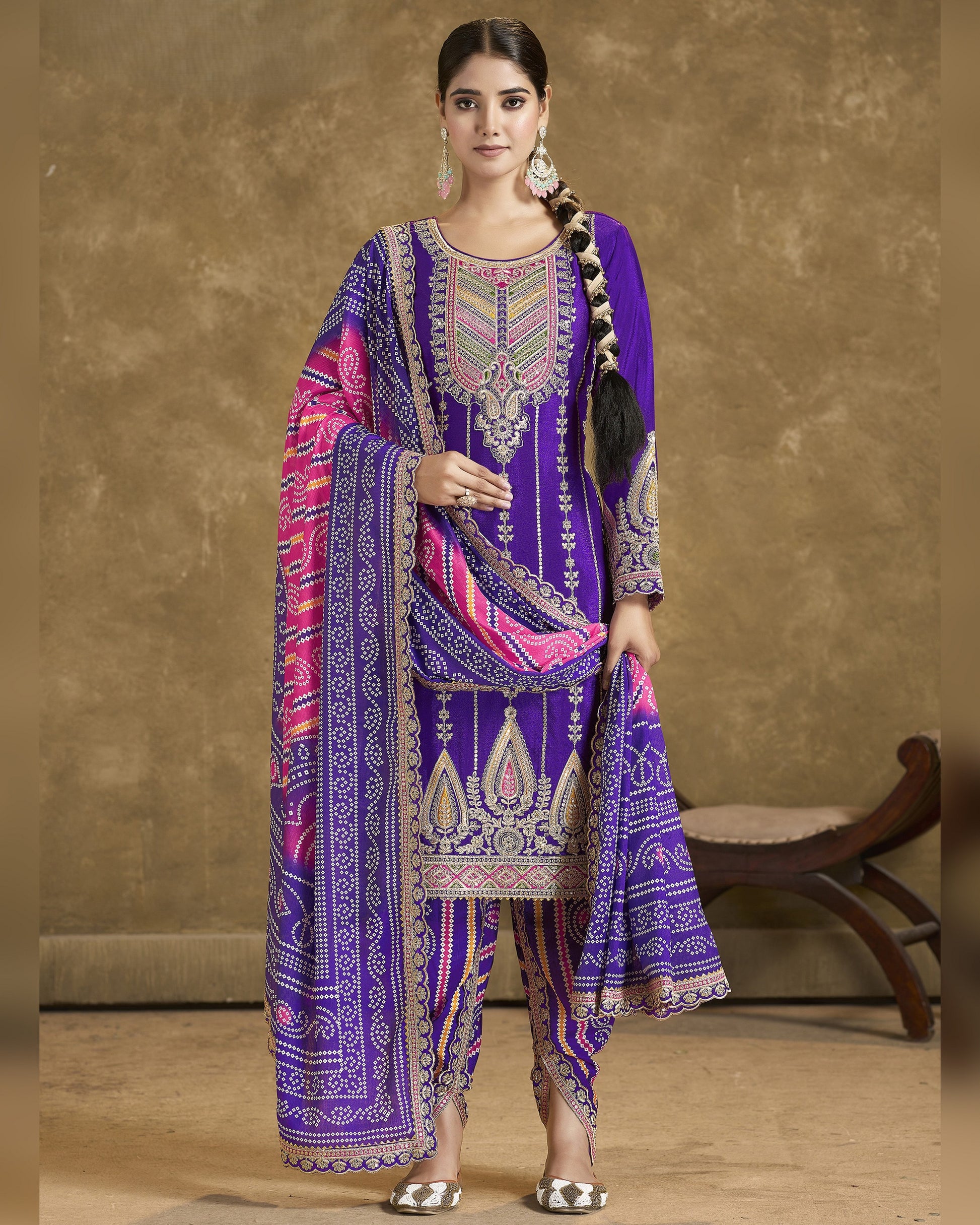 Woman wearing a traditional embroidered outfit with a purple and pink design against a beige background.