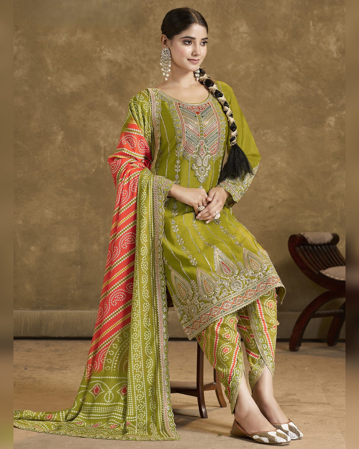 Woman wearing a green embroidered traditional outfit with a red and gold dupatta against a beige background