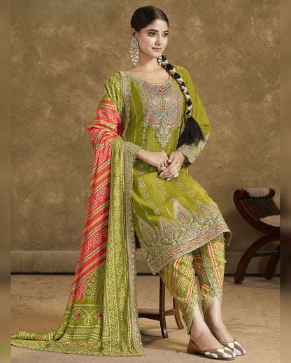 Woman wearing a green embroidered traditional outfit with a red and gold dupatta against a beige background
