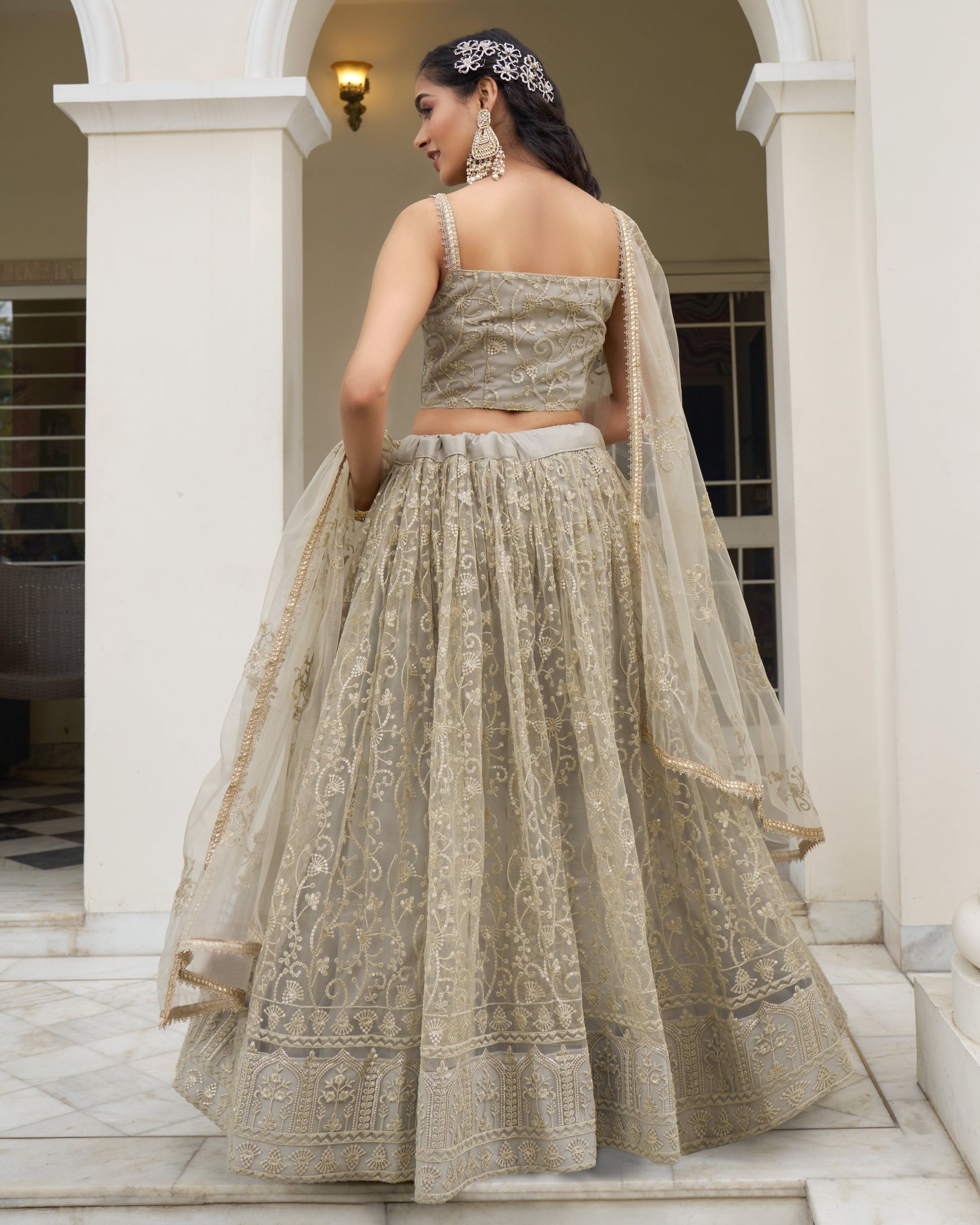 Woman in a traditional embroidered lehenga standing in an architectural setting.