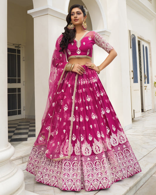 Woman in a pink embroidered traditional outfit standing in front of a white building.
