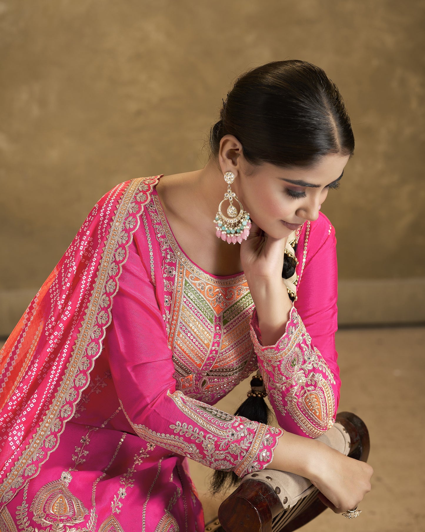 Woman in a traditional pink embroidered outfit with jewelry against a beige background