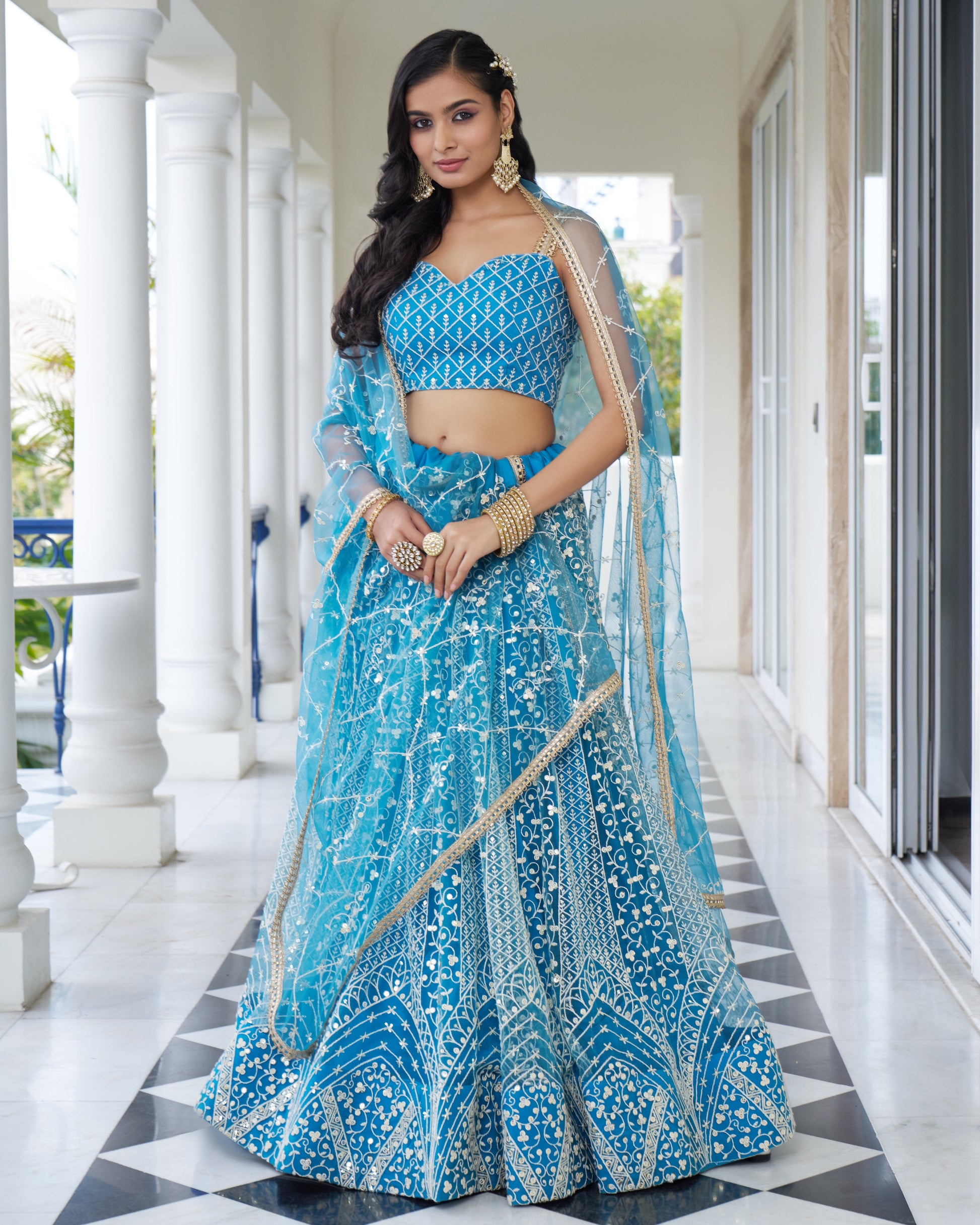 Woman in a blue traditional outfit standing in a well-lit room with white columns.