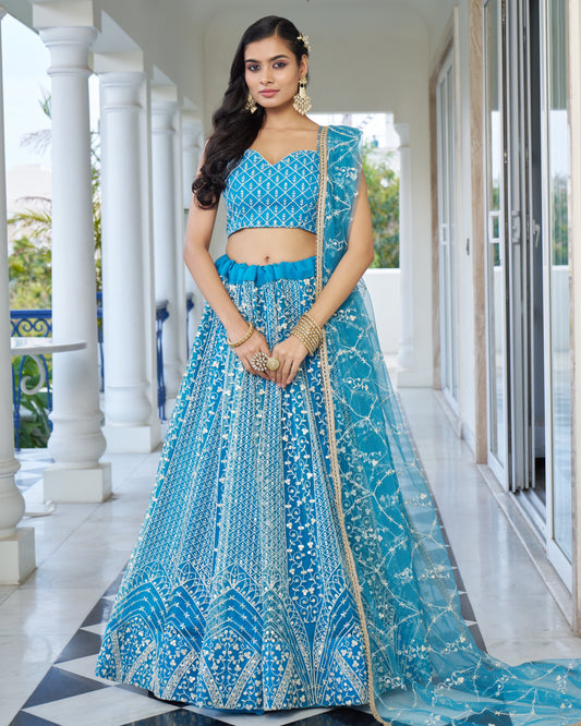 Woman wearing a blue traditional outfit with intricate patterns in an outdoor setting.