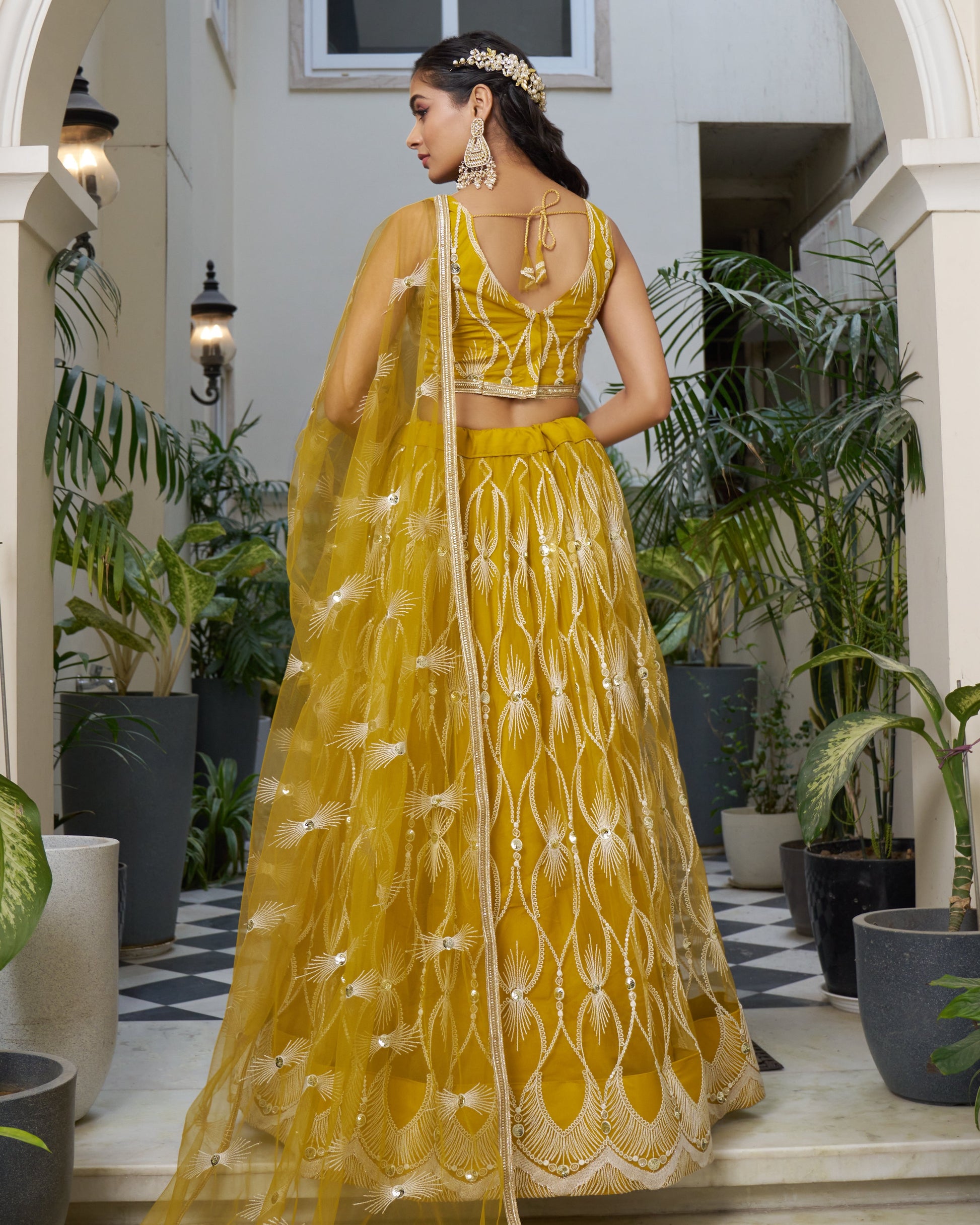 Woman in a yellow traditional outfit standing in an indoor setting with plants.