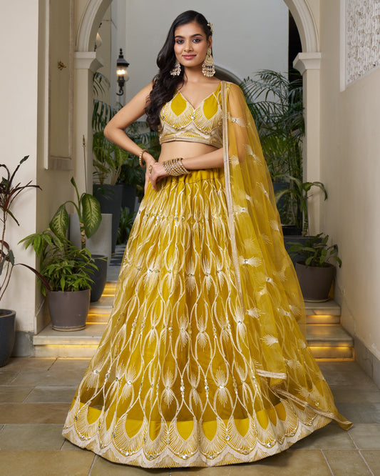 Woman in a yellow traditional outfit standing in an indoor setting with plants.