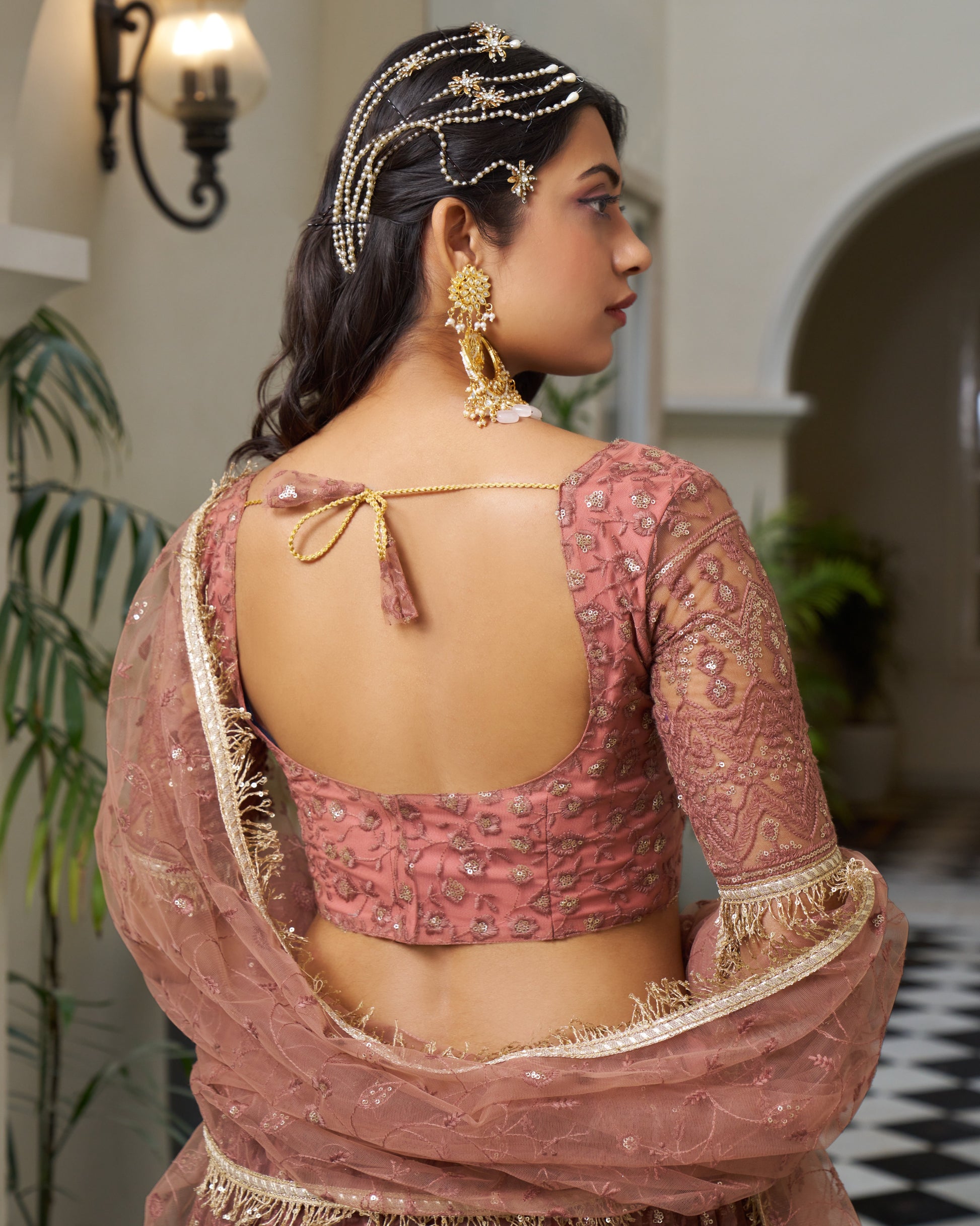 Woman wearing a traditional pink blouse with intricate designs and gold detailing.