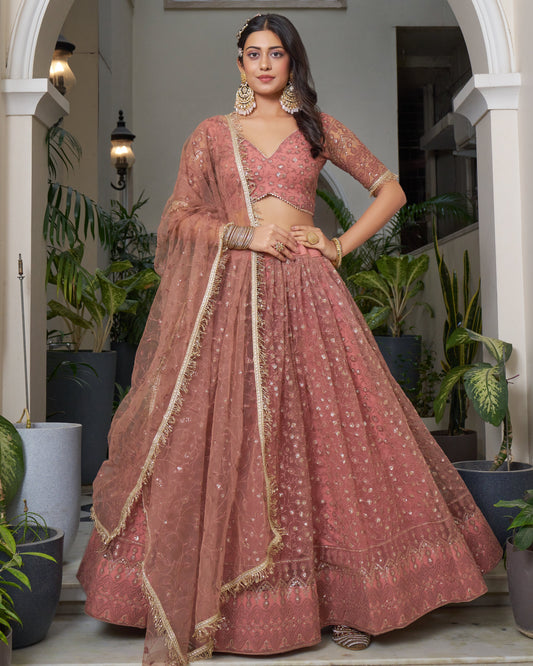 Woman in a traditional pink lehenga with gold details standing in an indoor setting with plants.