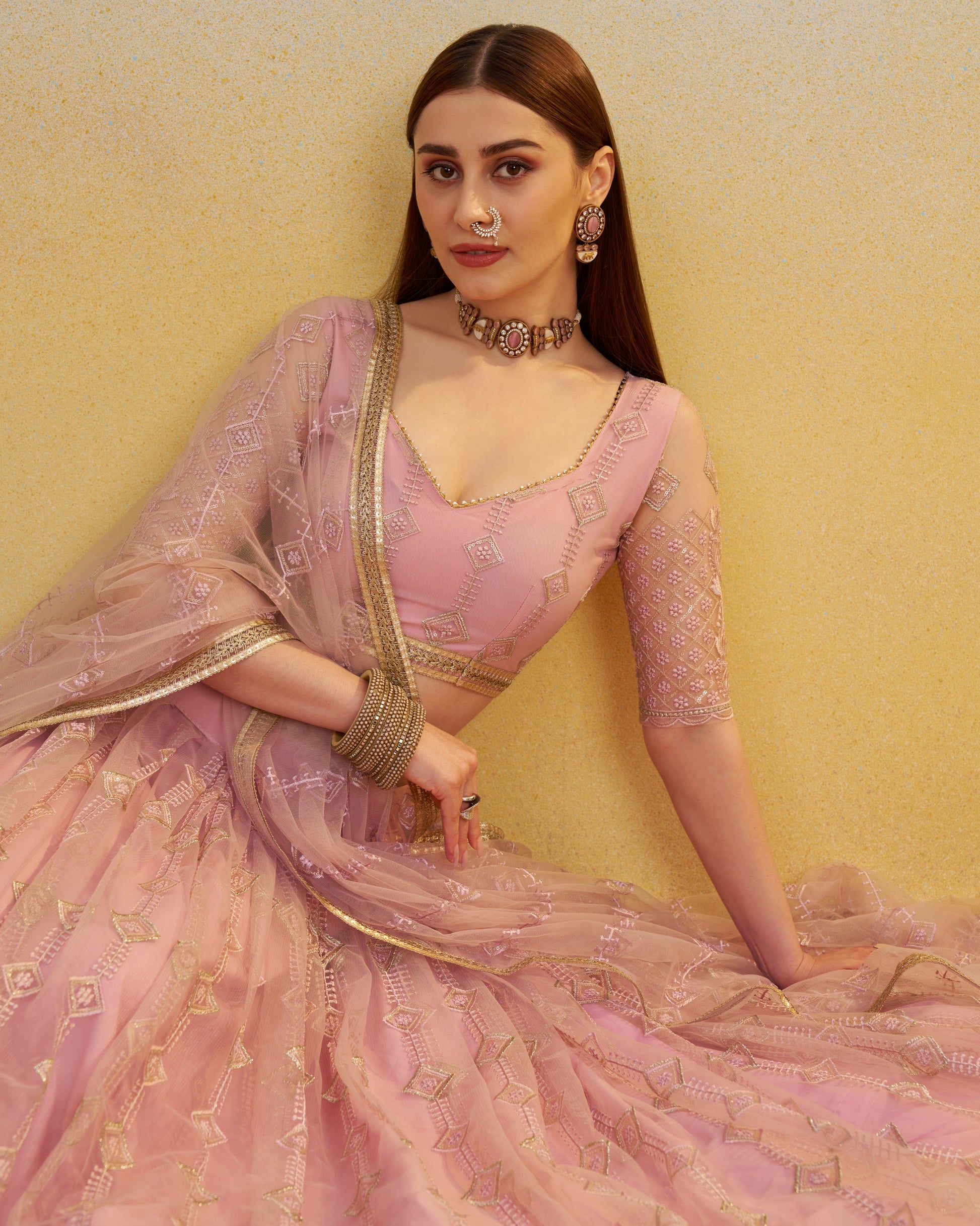 Woman in a pink saree with gold details against a yellow background