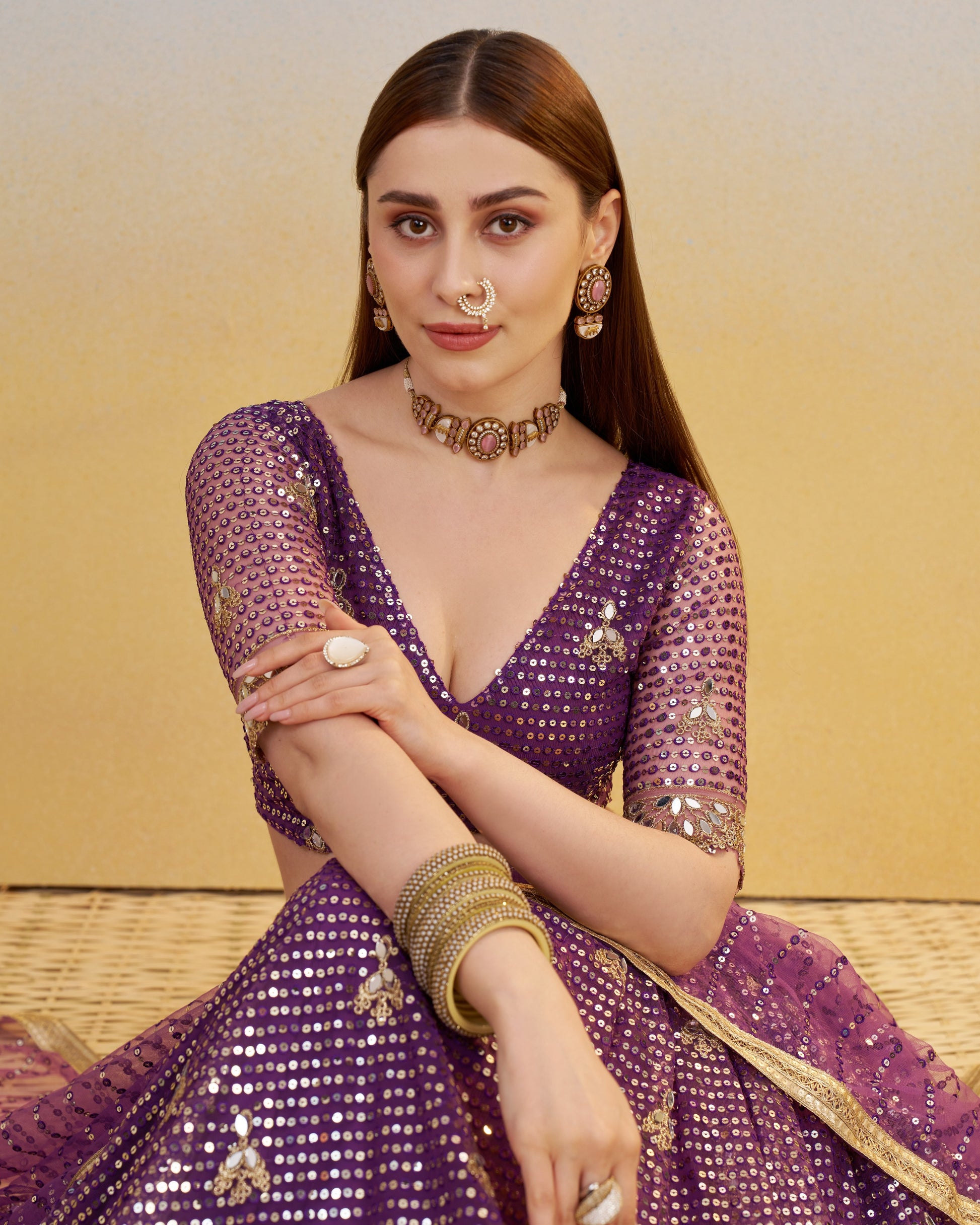 Woman in a purple traditional outfit with gold jewelry against a yellow background