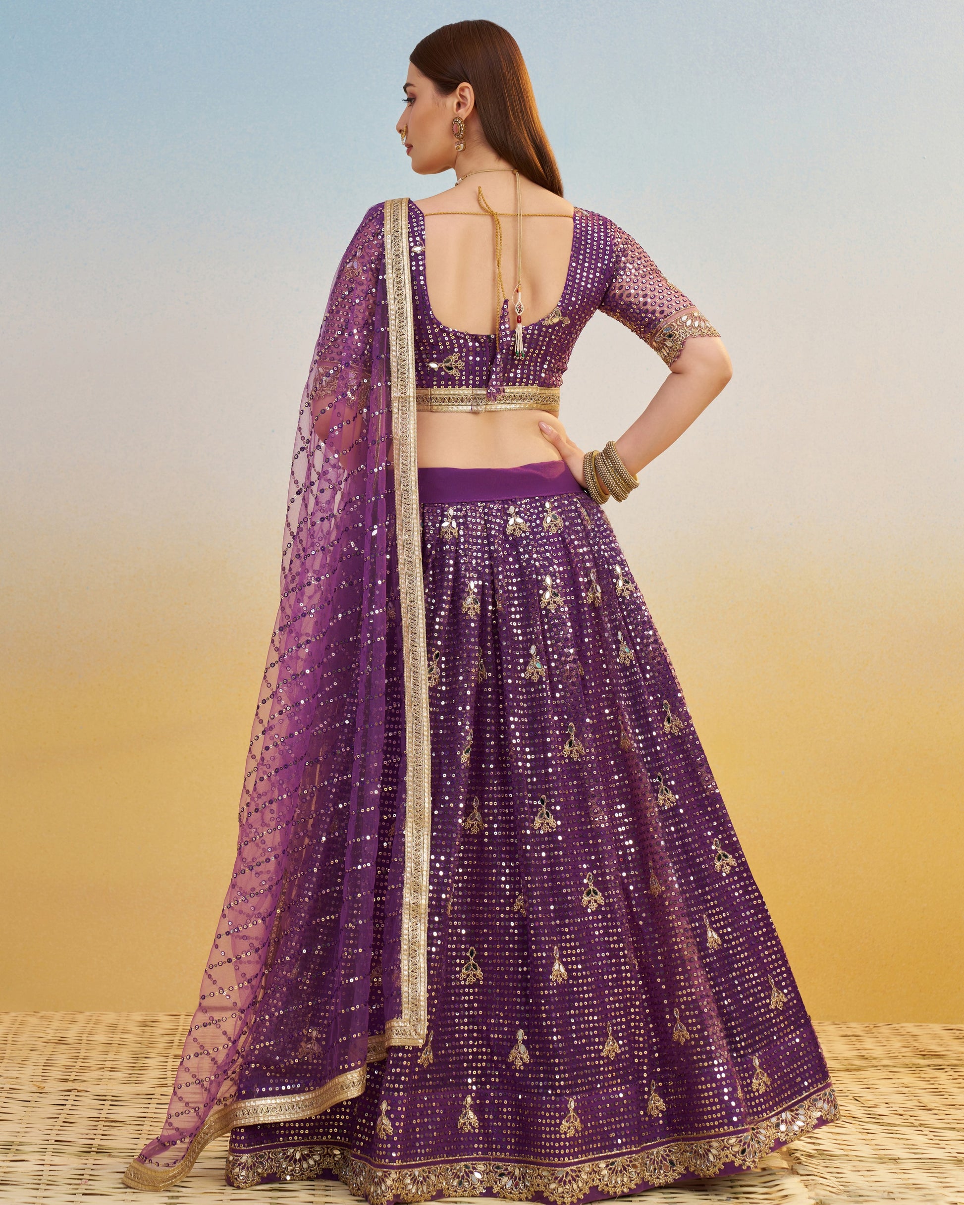 Woman wearing a purple embroidered lehenga with a gold blouse against a gradient background