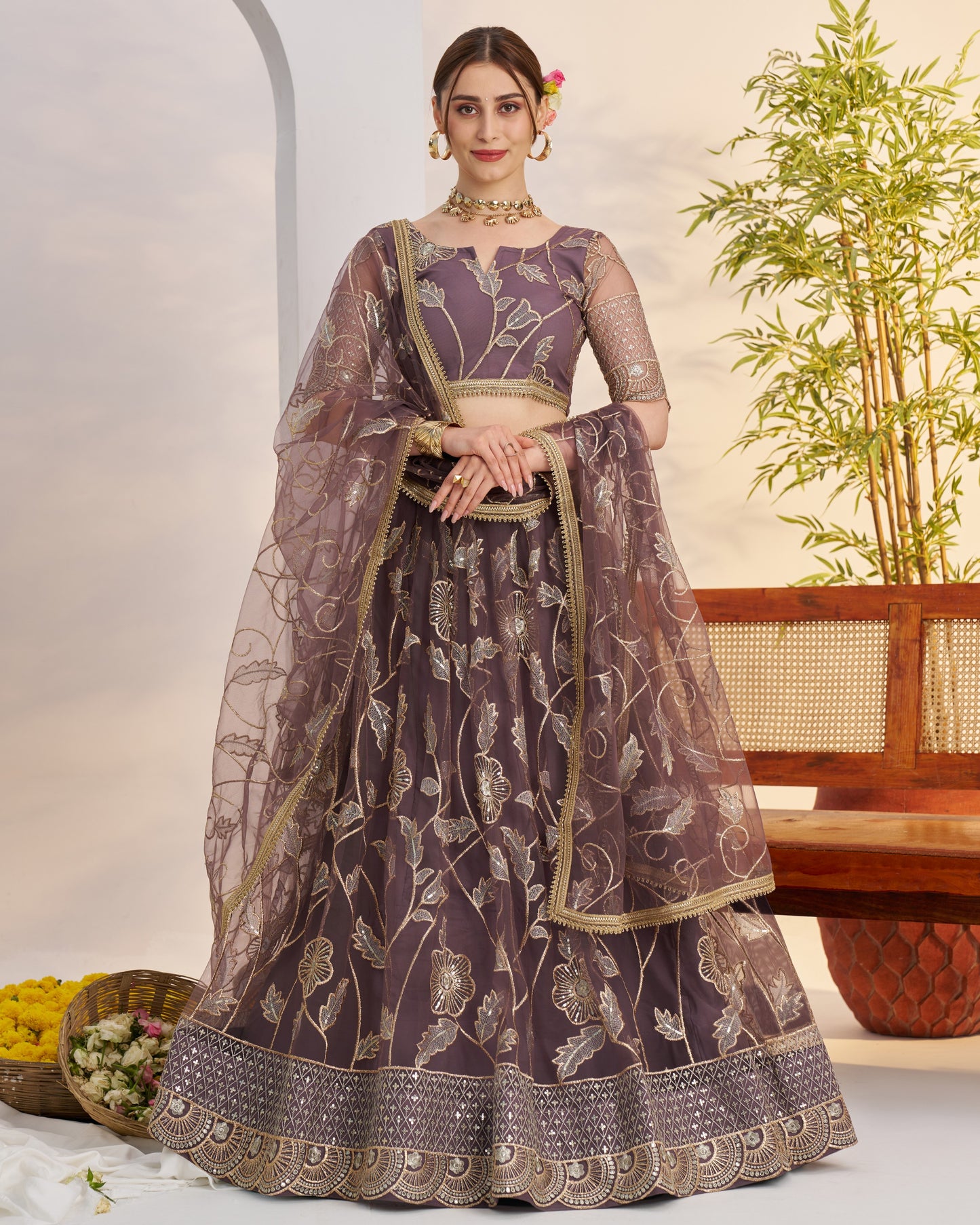 Woman wearing a traditional purple and gold embroidered lehenga with a plant in the background