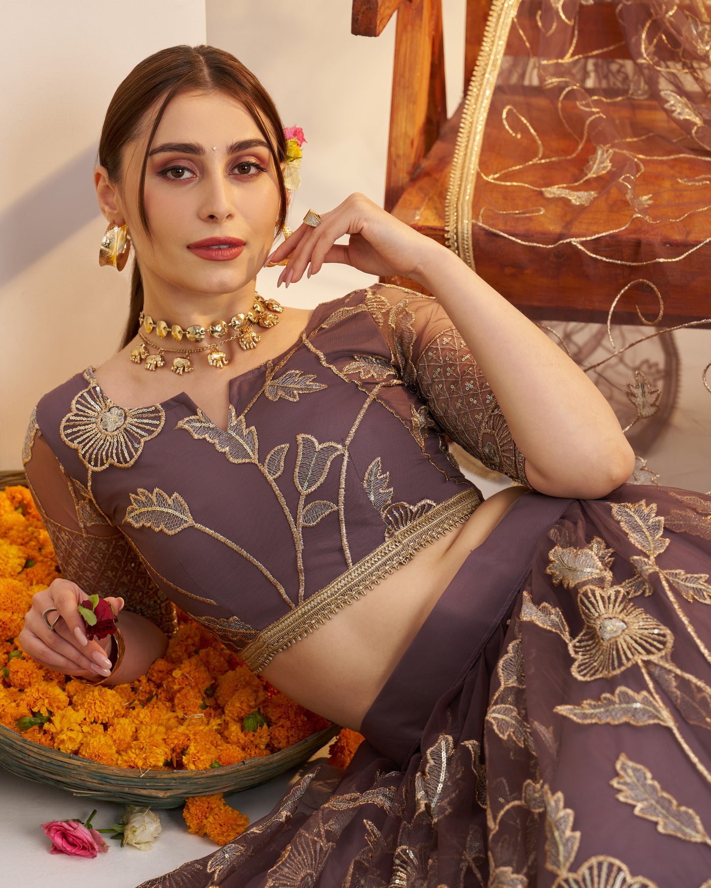 Woman in a traditional embroidered saree sitting on a floral carpet with a decorative background