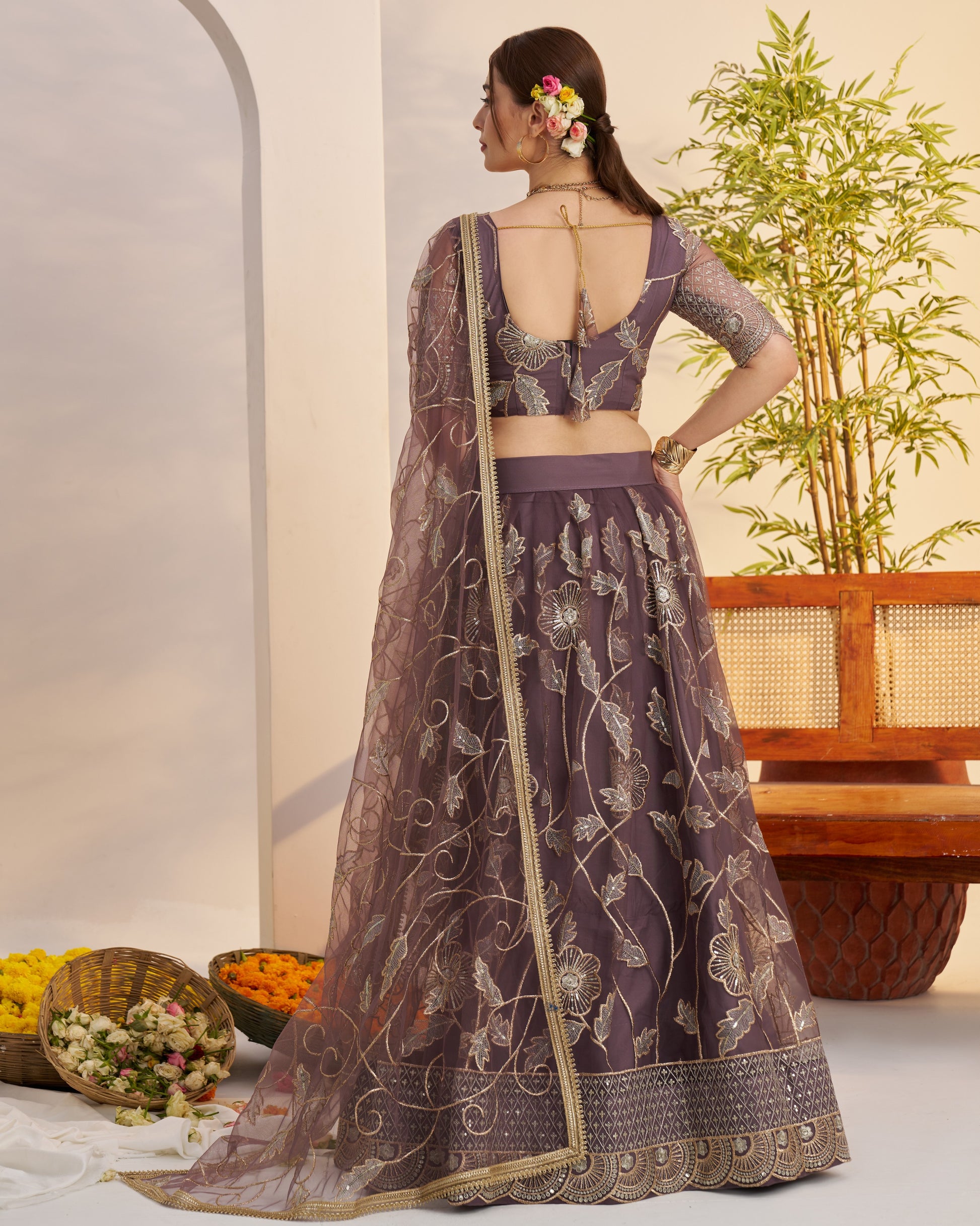Woman in a purple embroidered lehenga with a floral arrangement in her hair, standing against a neutral background.
