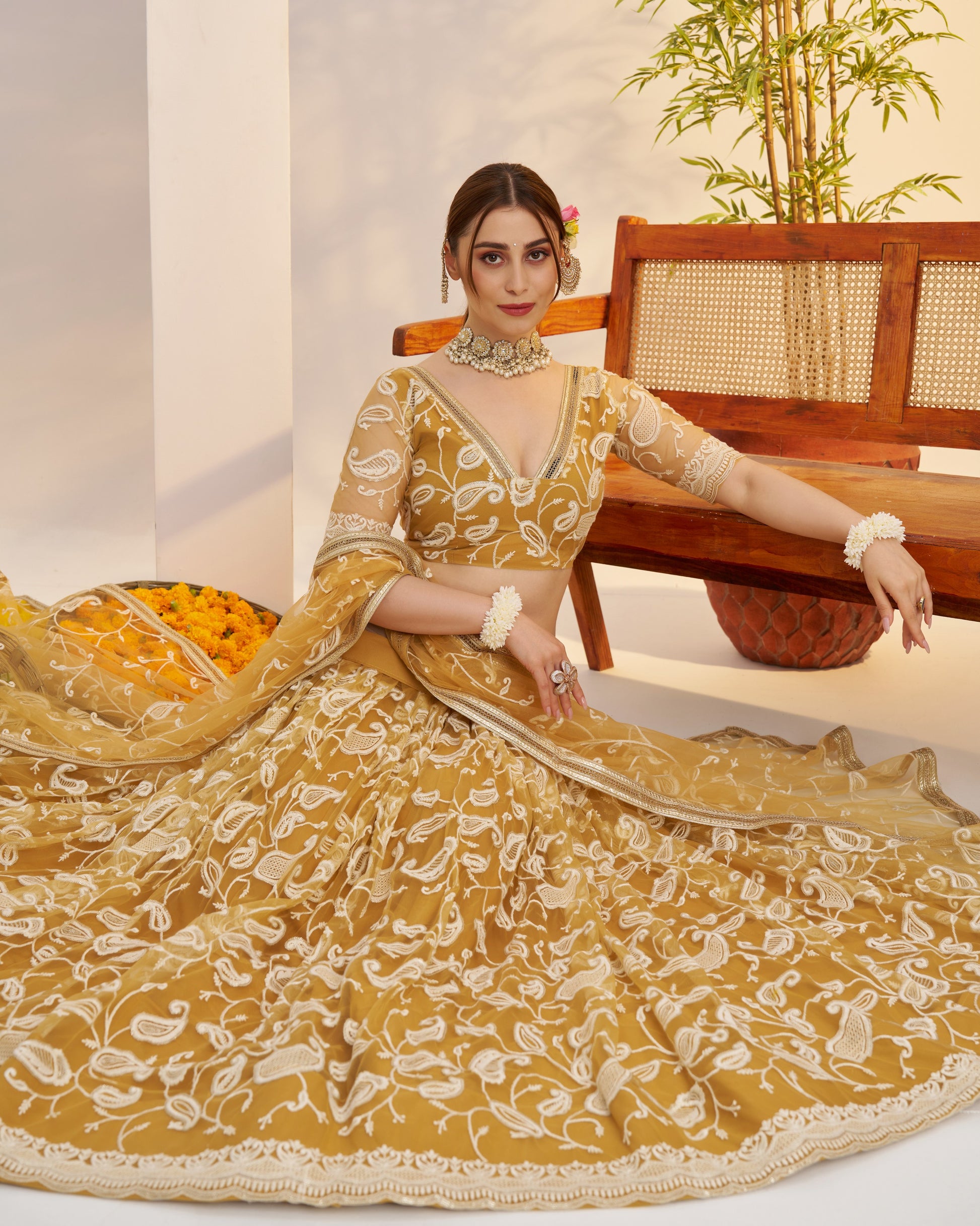 Woman in a yellow and white embroidered traditional outfit sitting on a wooden chair.