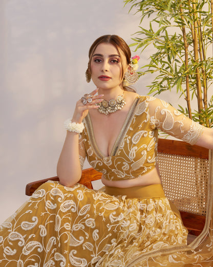 Woman in a yellow and white traditional outfit with jewelry, sitting on a chair.