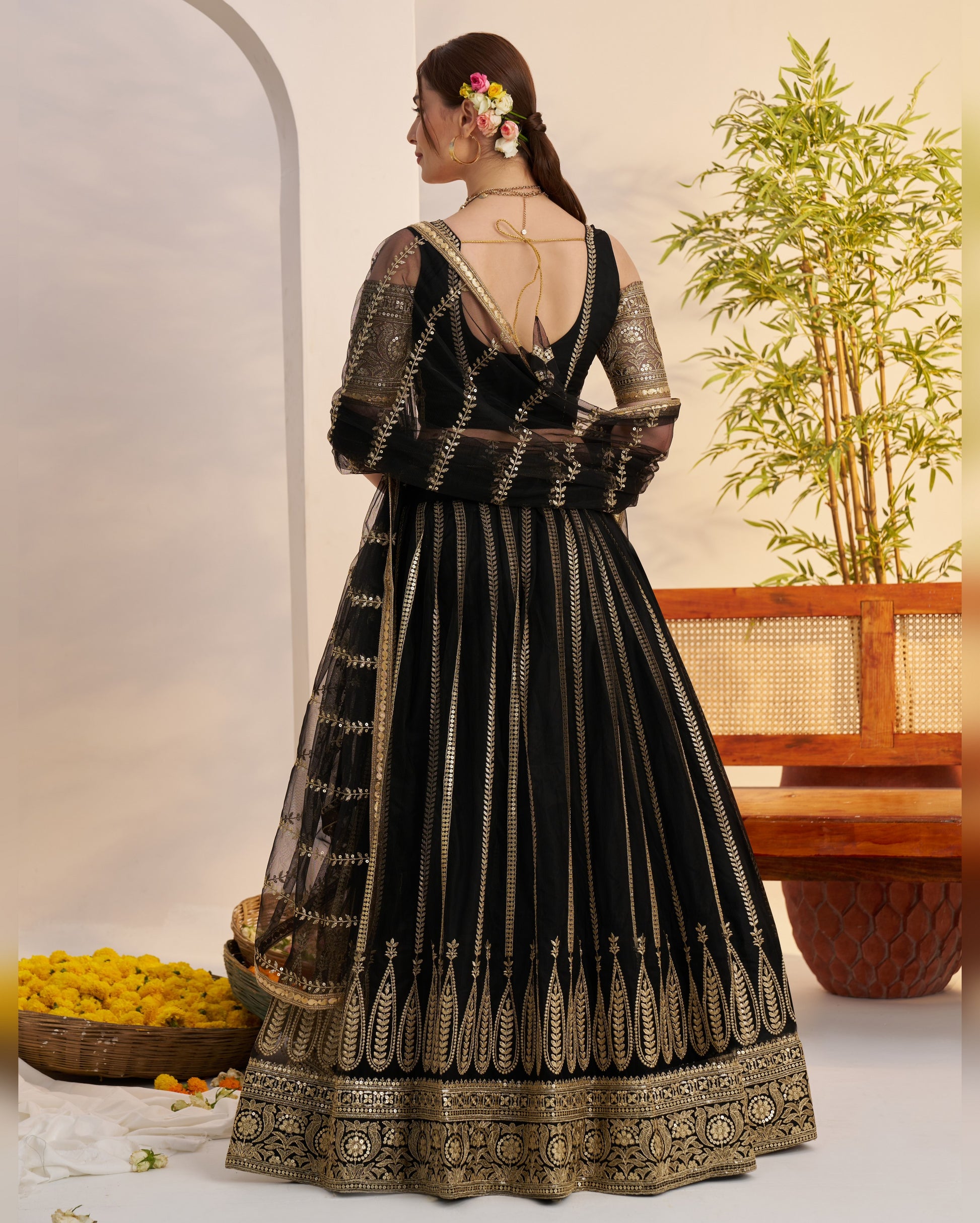 Black and gold embroidered traditional outfit with a plant and decorative elements in the background
