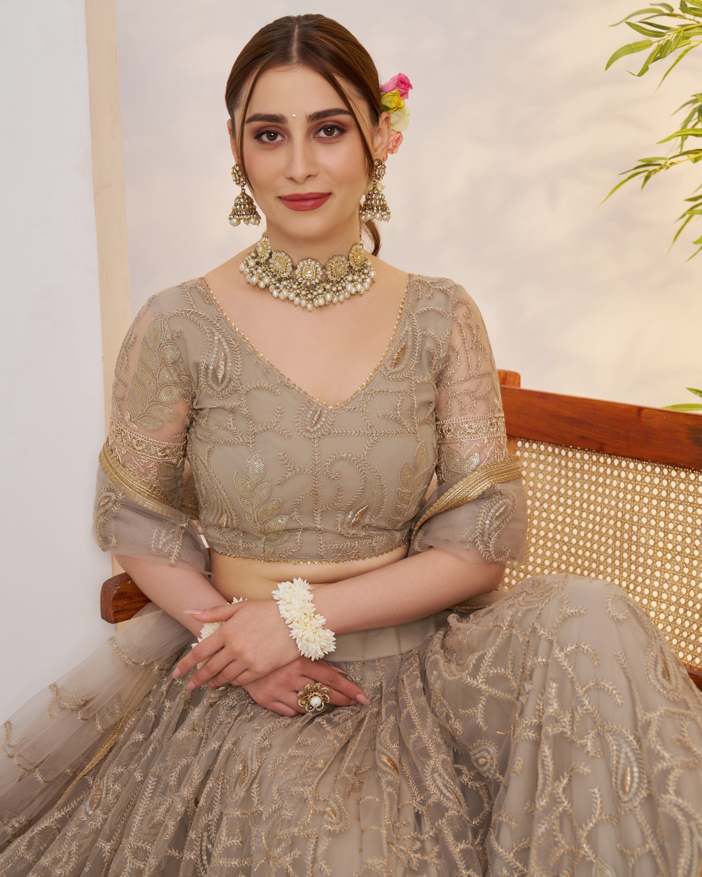 Woman in traditional attire with jewelry, sitting on a chair.
