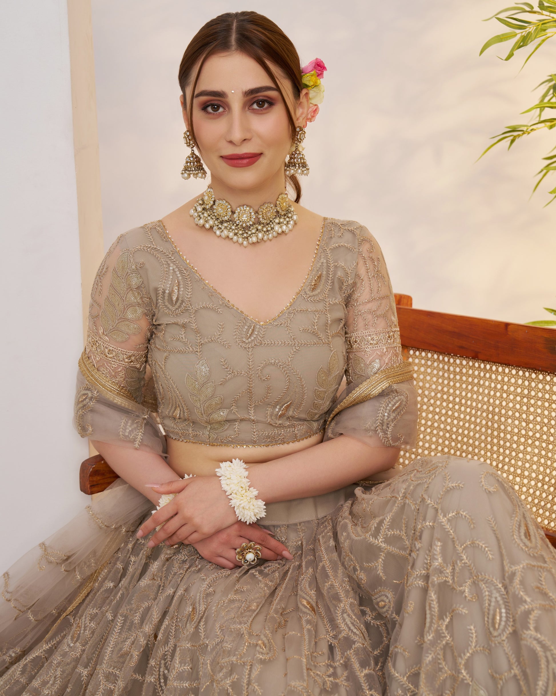 Woman in traditional attire with jewelry, sitting on a chair.