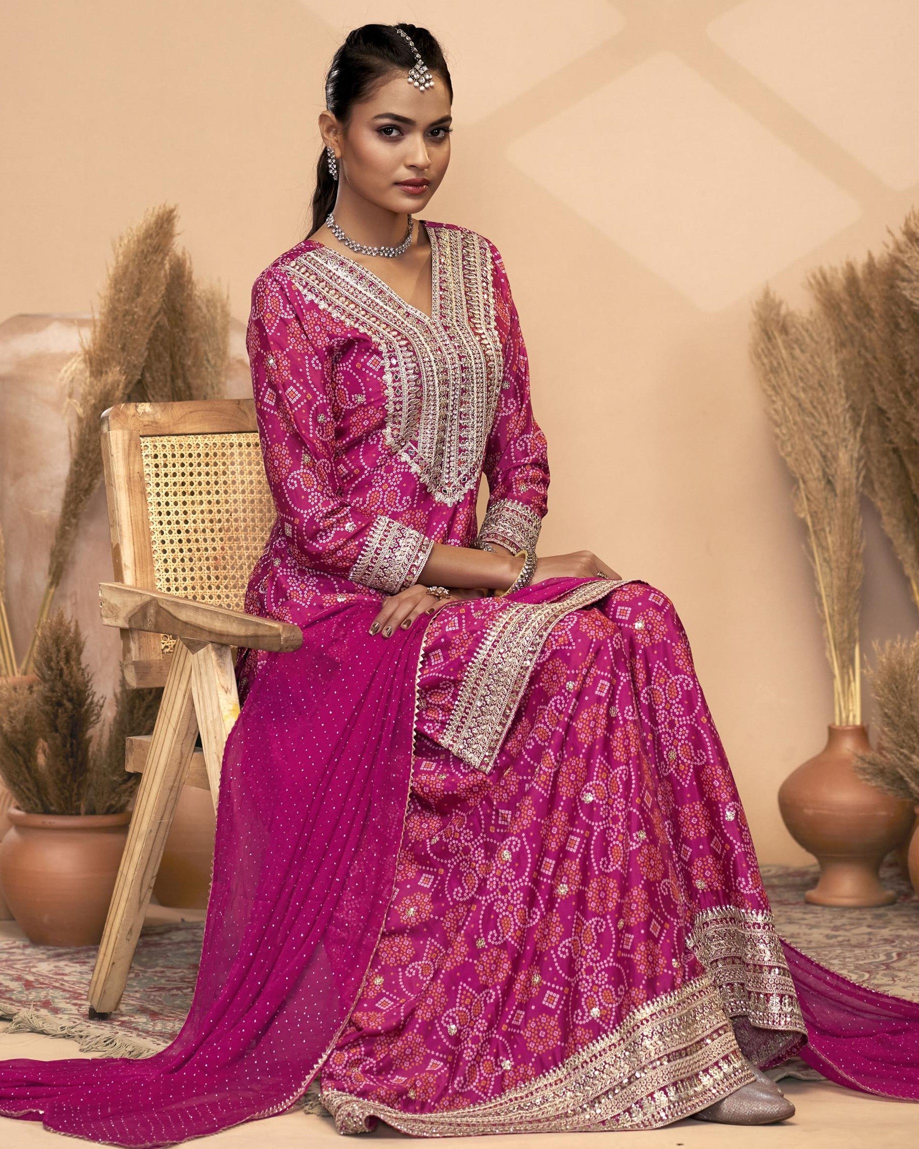Woman in a traditional pink and silver embroidered outfit sitting on a wooden chair.