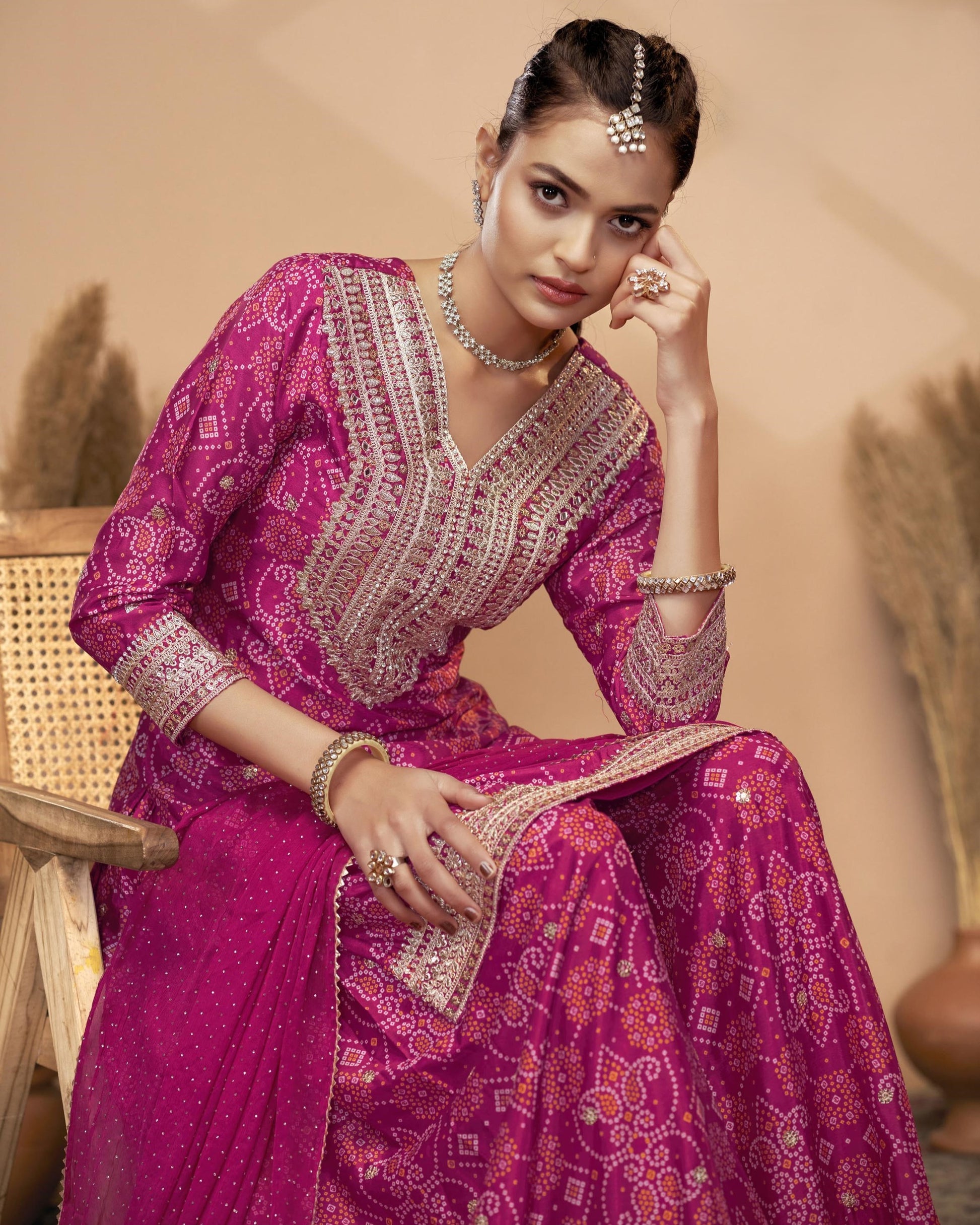 Woman in a traditional pink embroidered outfit sitting on a chair.