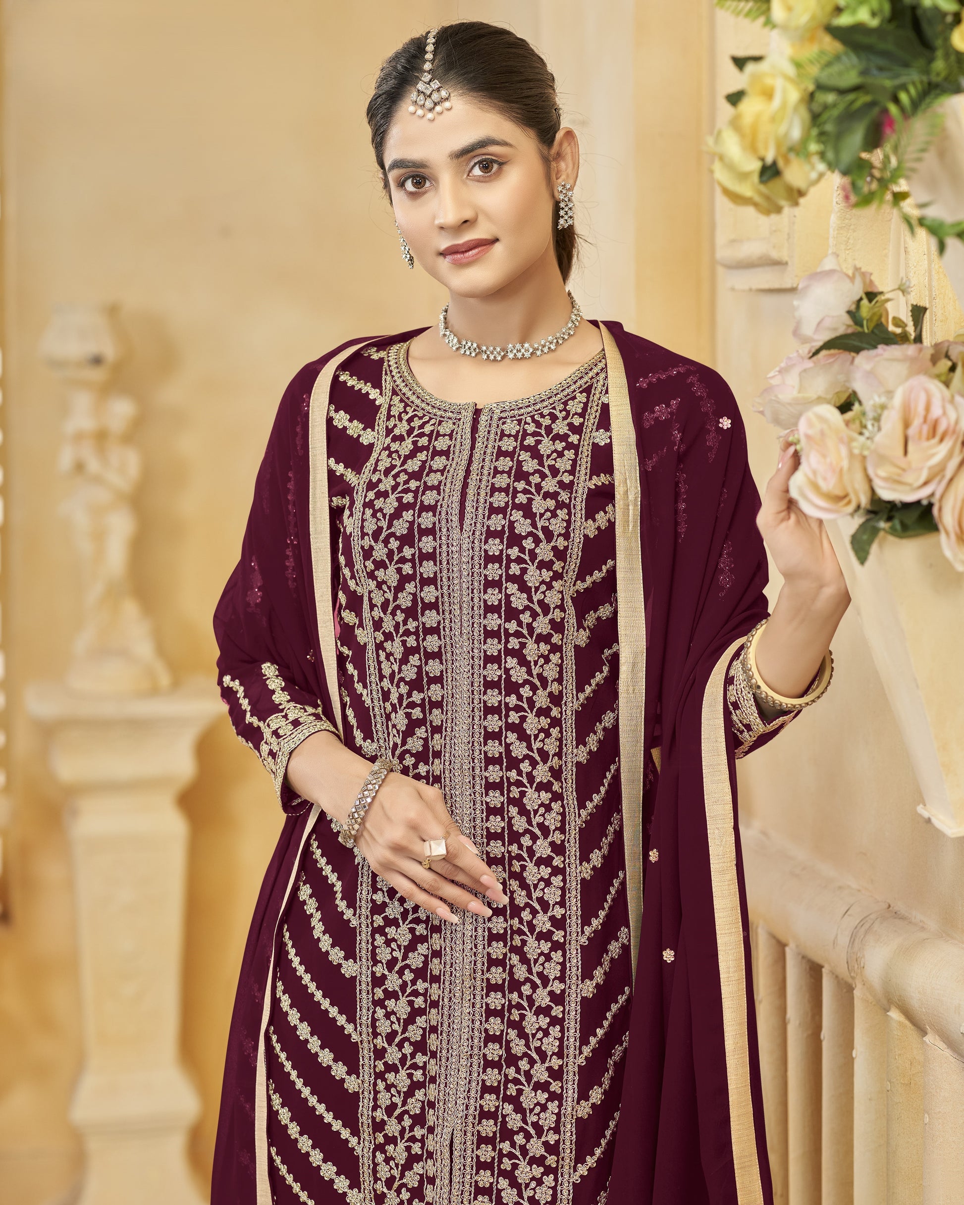 Woman in a traditional embroidered outfit with jewelry, standing indoors.