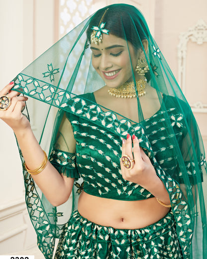 Woman wearing a green traditional outfit with a matching veil indoors.