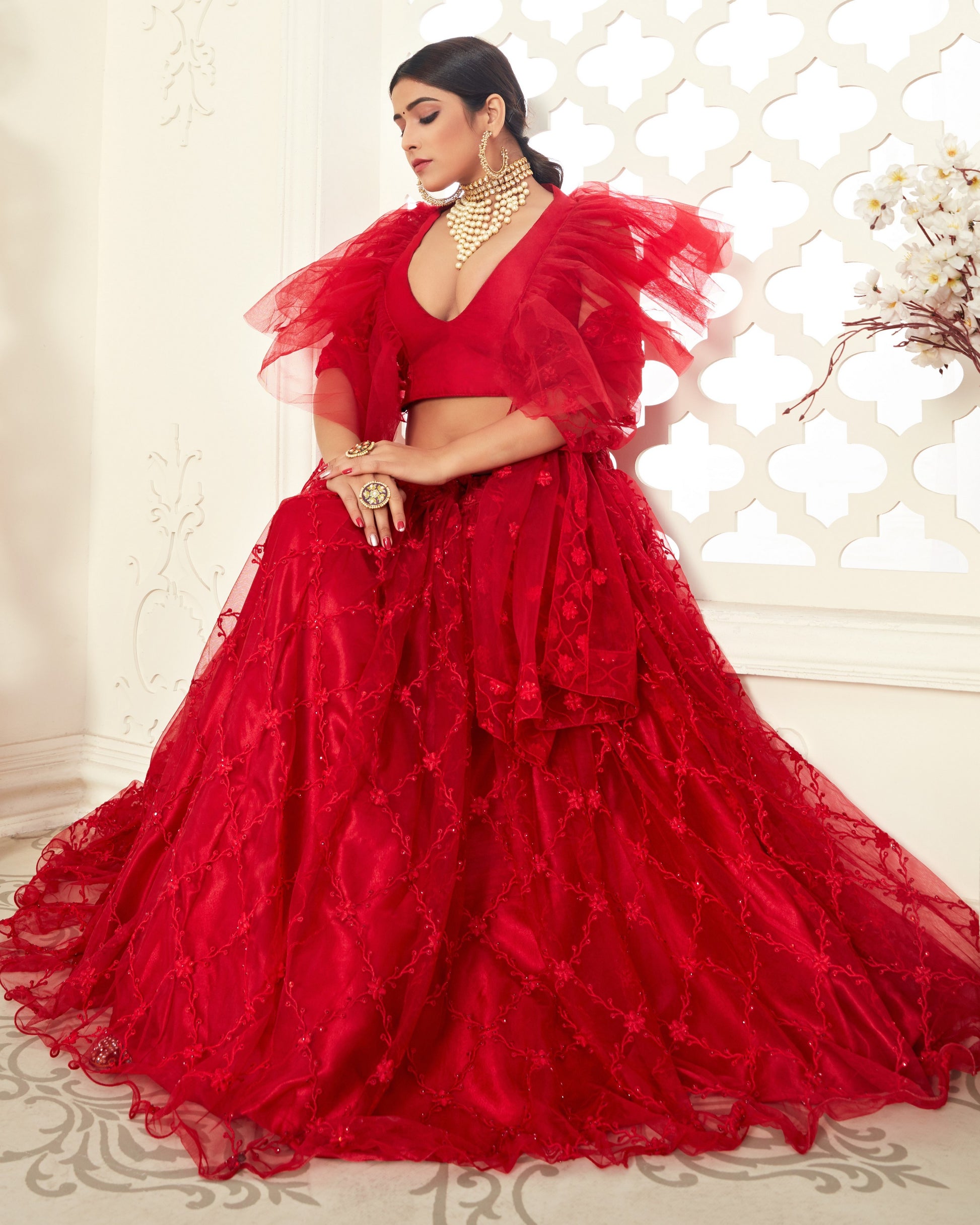 Woman wearing a red, layered dress with a white decorative wall in the background