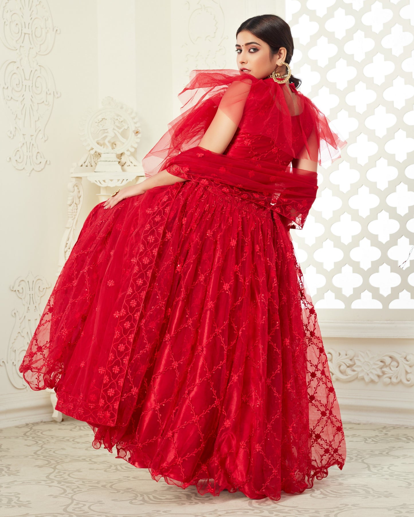 Woman in a red lace dress sitting on a white chair with a decorative white wall background