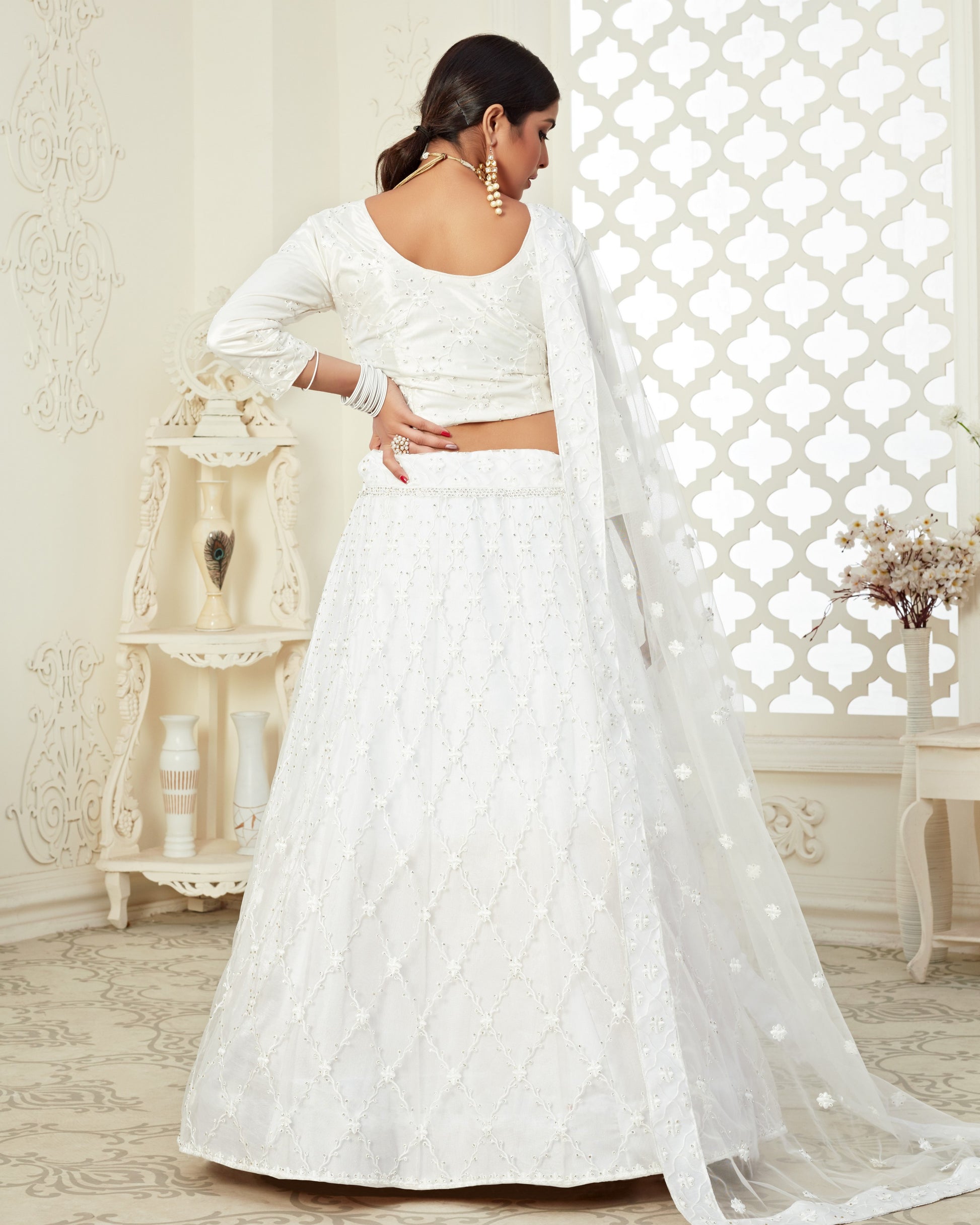 Woman wearing a white embroidered lehenga in a decorated room.