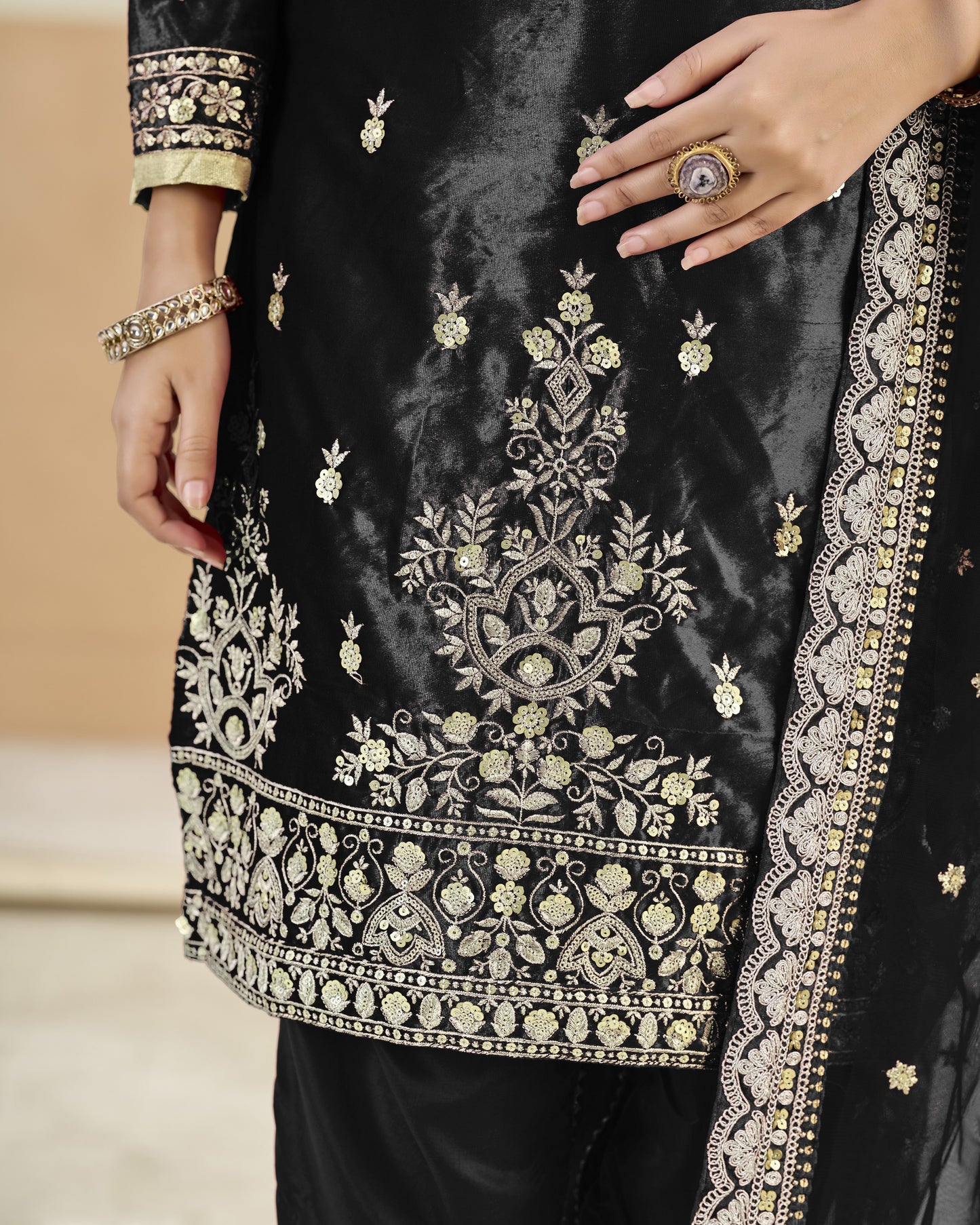 Black embroidered garment with gold detailing on a neutral background