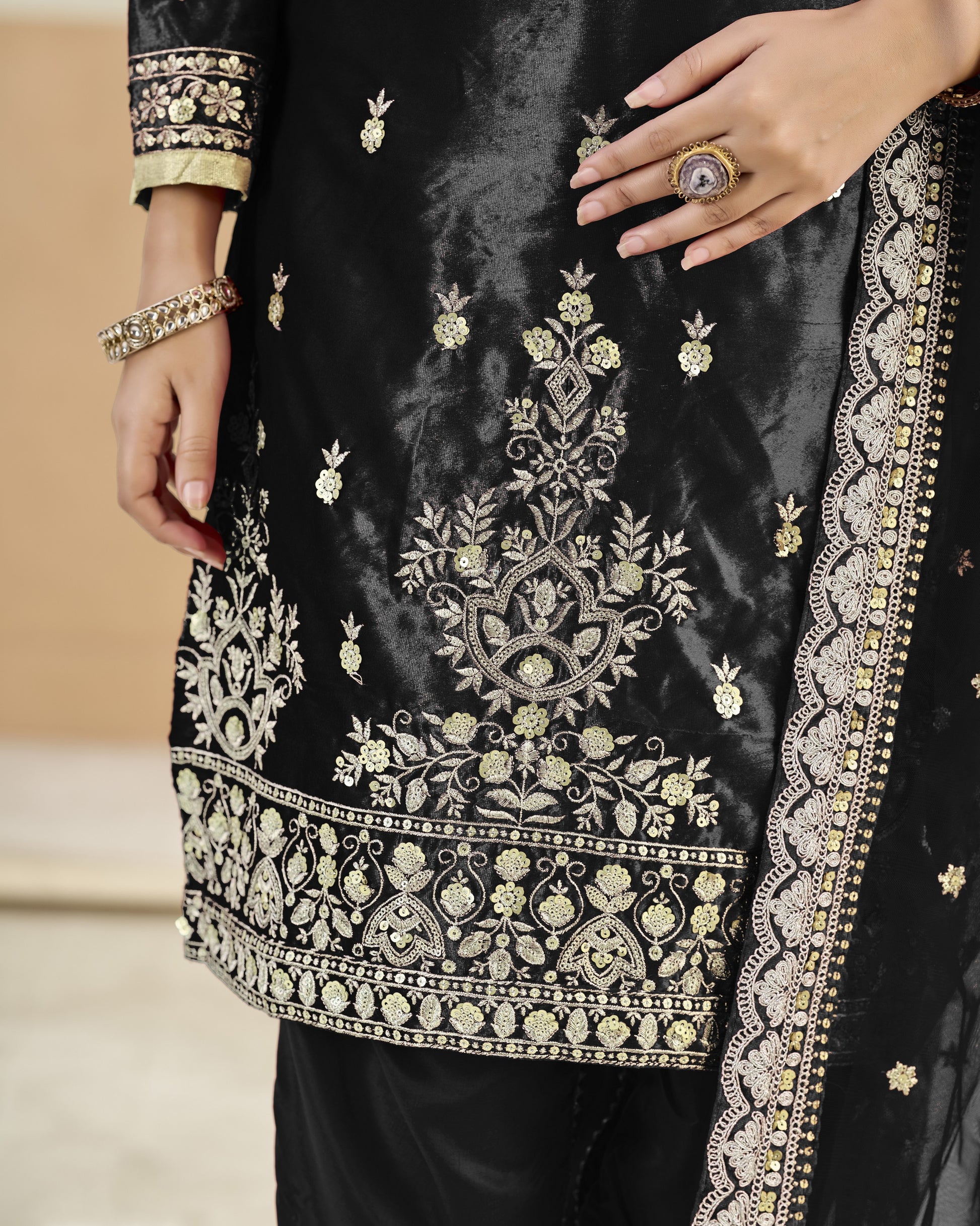 Black embroidered garment with gold detailing on a neutral background